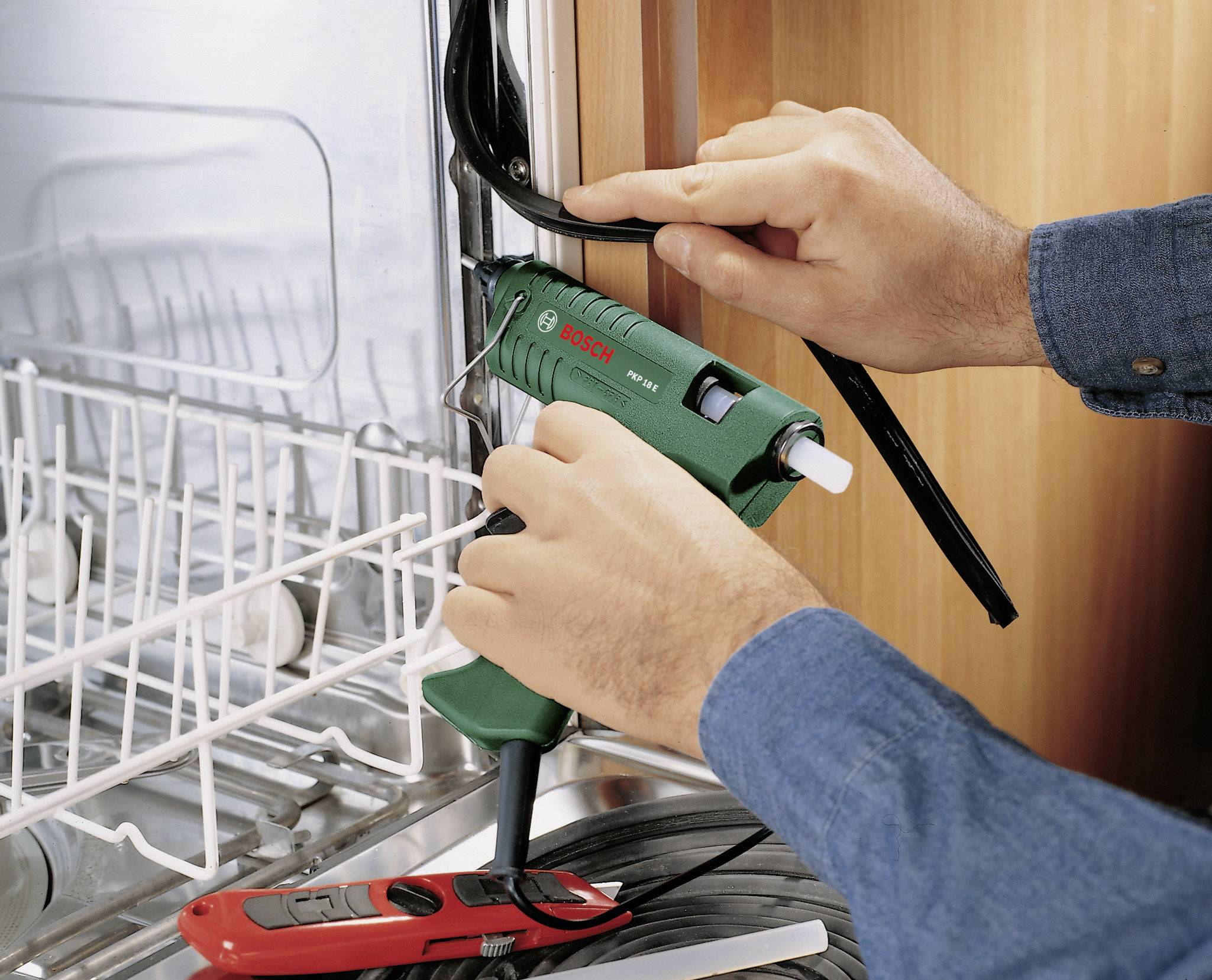 Oseba popravlja pomivalni stroj s pištolo za vroče lepljenje, da bi namestila tesnilo.