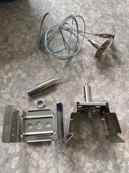 Kovinski deli in žice ležijo na vzorčasti površini. Videti so sponke, kabel z dvema priključkoma in adapter za vijake.
