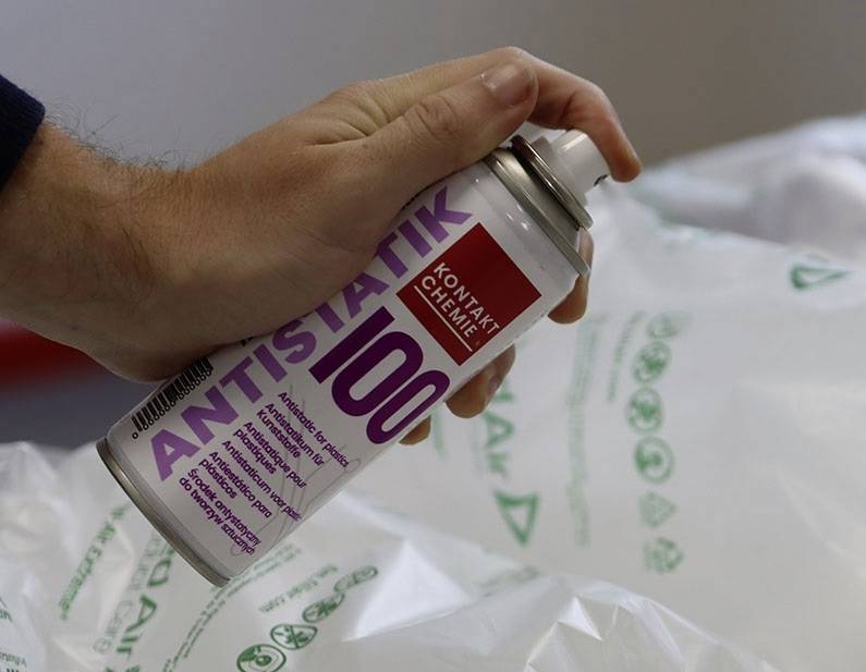 En hand håller en sprayburk 'Antistatik 100' över plastmaterial.
