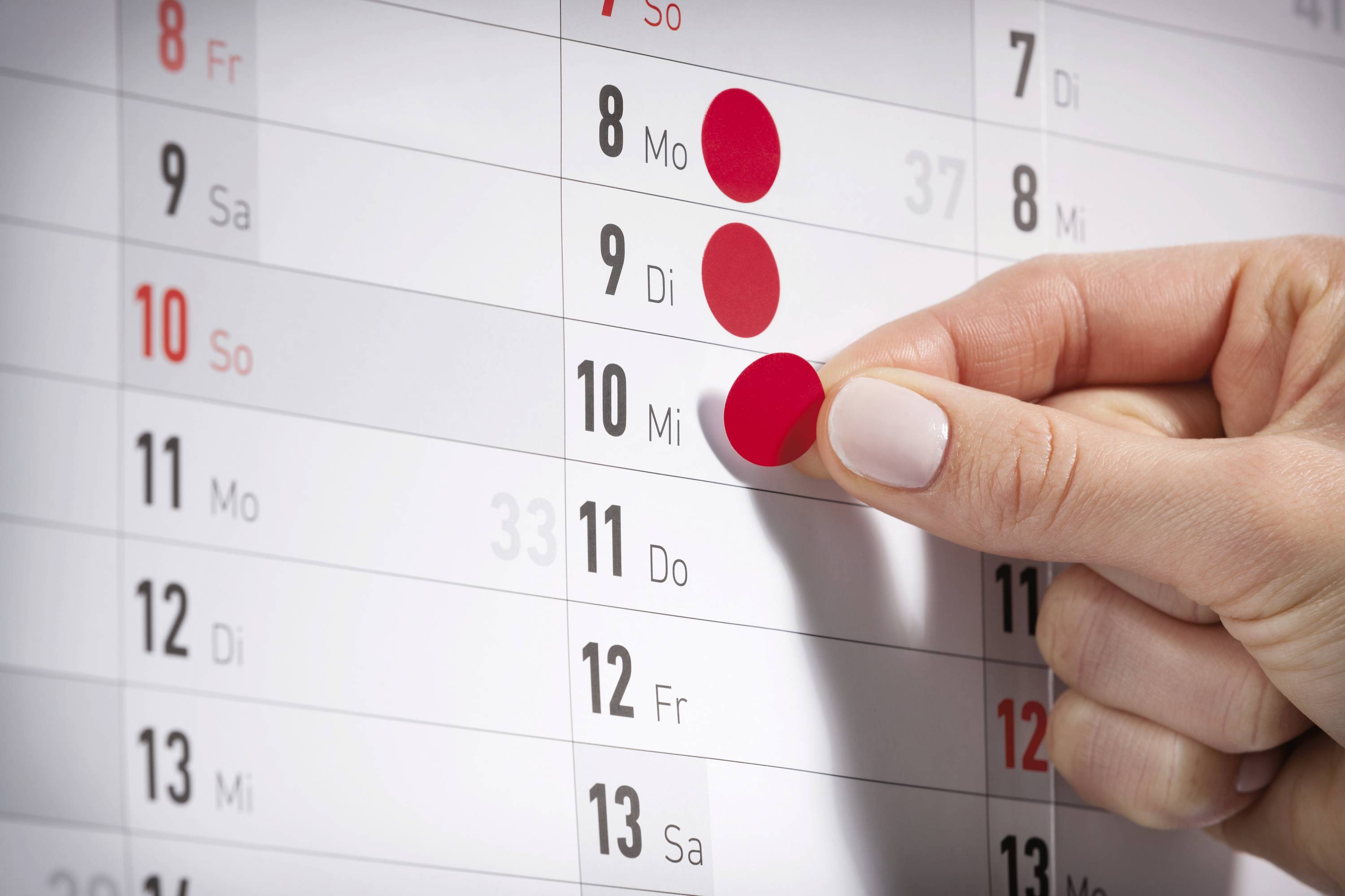 En hand markerar den 10 mars på en väggkalender med en röd punkt.