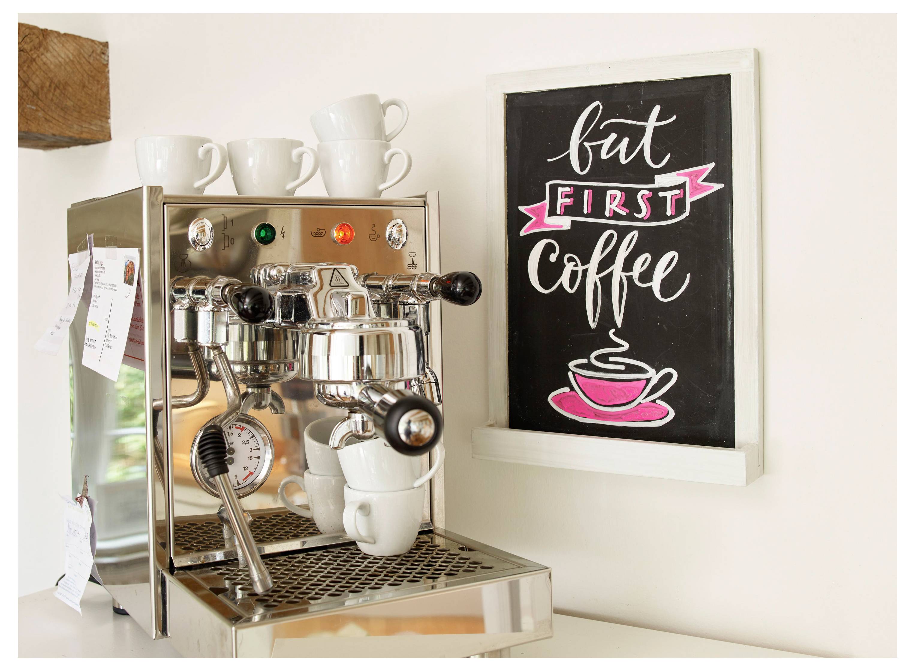 Kaffebryggare på ett bänkskiva bredvid en inramad skylt som läser "men FÖRST Kaffe" med en rosa koppillustration.