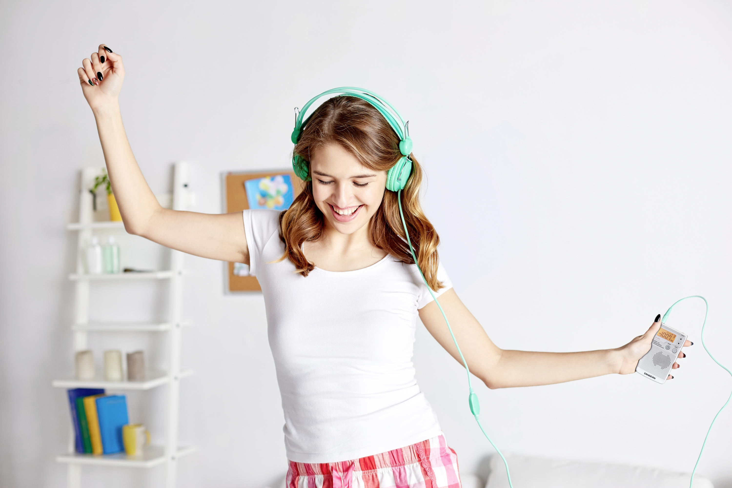 En ung kvinna dansar glatt i sitt rum, har hörlurar på sig och håller en musikspelare i handen.