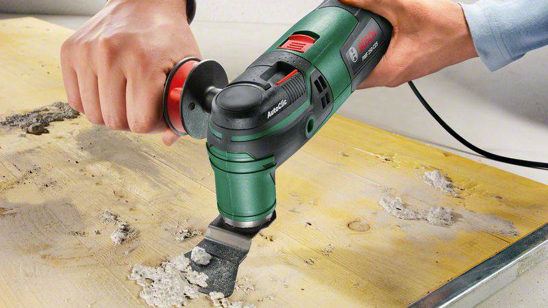 En person använder ett oscillerande elverktyg för att ta bort kakelfix från en träyta.