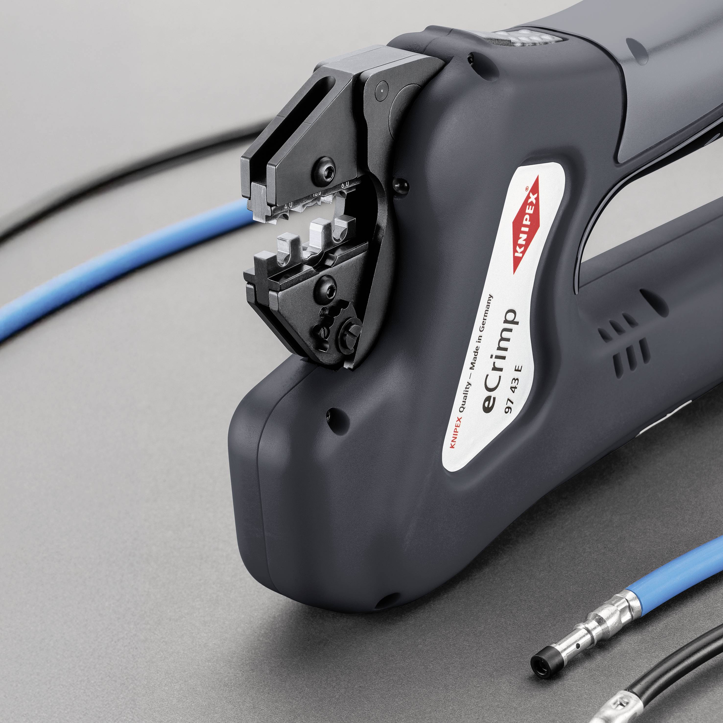 Elektriskt krympverktyg med blå kabel, redo att krympa. Verktygets märke och modellnummer synliga på framsidan.