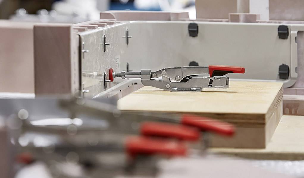 Metalliska klamrar håller ett träbräde i en industriell miljö.