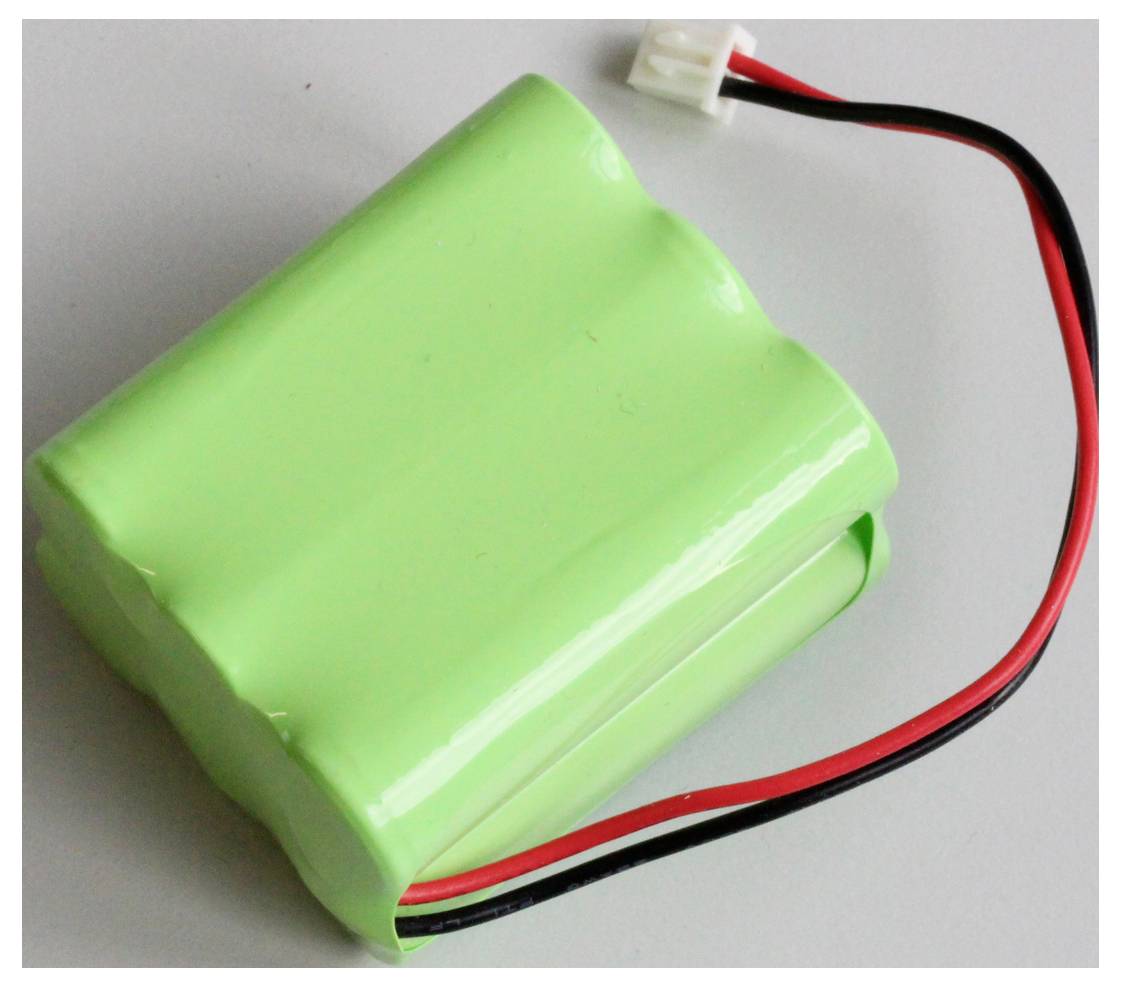 Grön batterienhet med rött och svart kabel, på vit bakgrund.