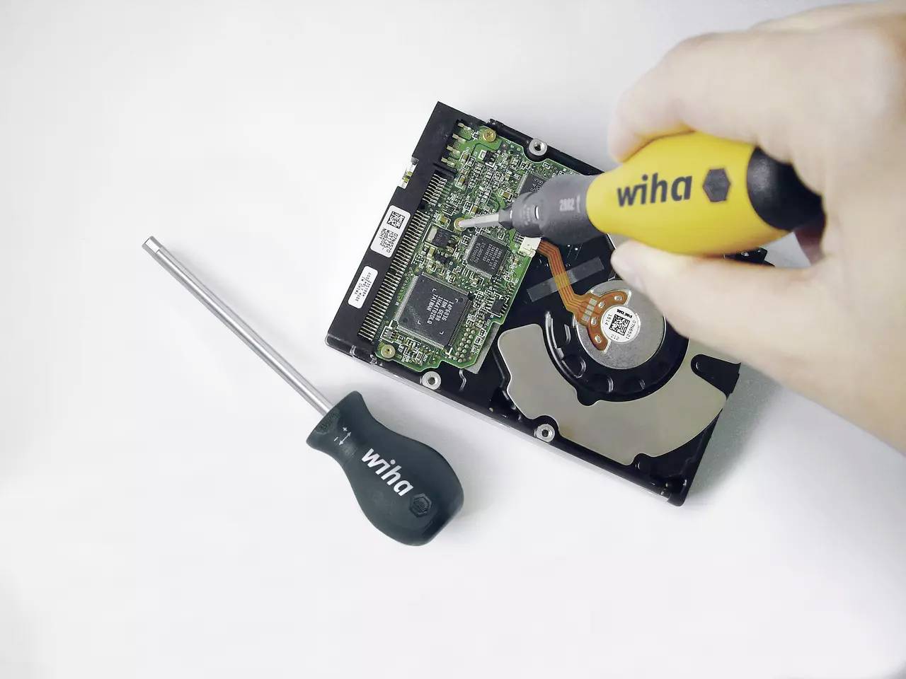 Närbild av en hand som arbetar med en skruvmejsel på en öppen hårddiskenhet, visar elektroniskt underhåll.