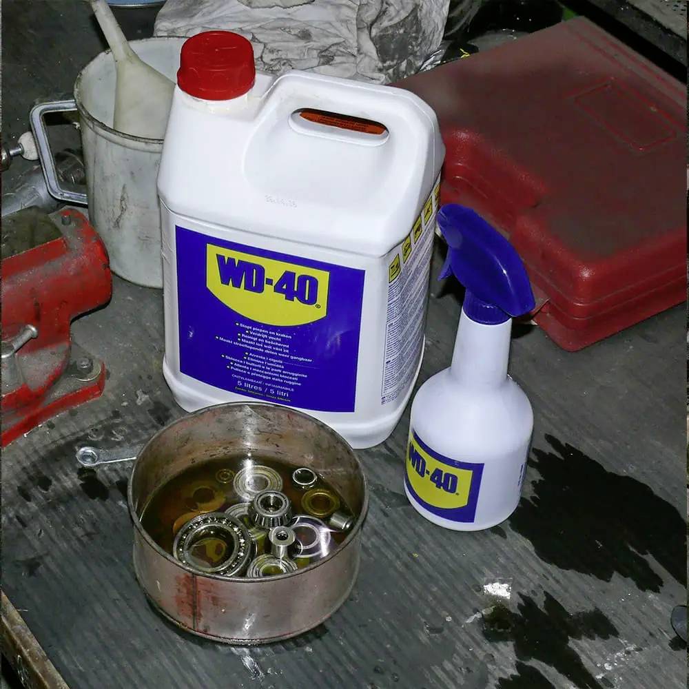 En öppen burk med metalldelar står på en arbetsbank. Bakom den finns en stor vit dunk och en sprayflaska med WD-40.