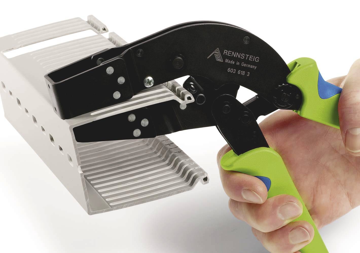 En hand håller en grön-svart tång med inskriptionen 'RENNSTEIG', som bearbetar en grå metallstruktur.