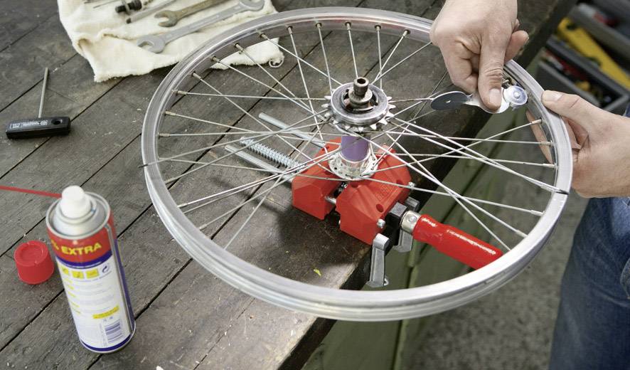 En person reparerar ett cykelhjul på en arbetsbank med verktyg, inklusive en sprejburk och skiftnycklar.