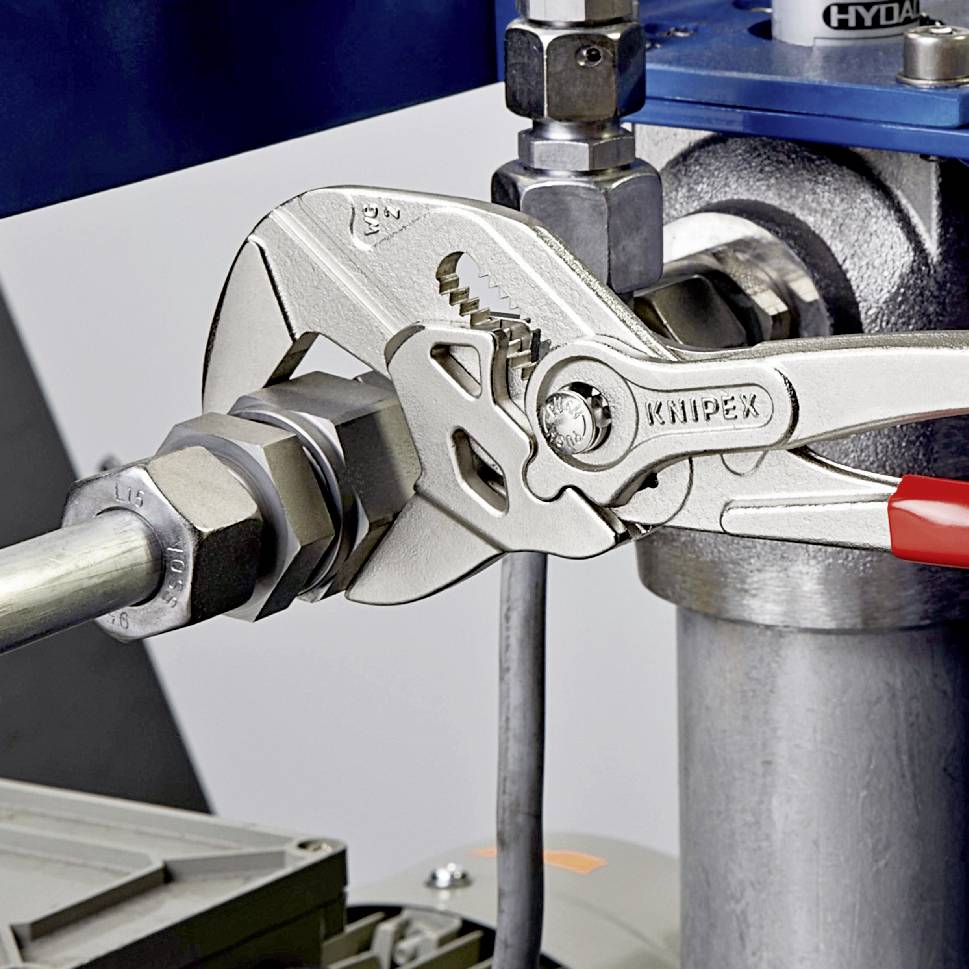 En rörtång håller fast en metallmutter på ett rör. Tången visar märket 'KNIPEX'. I bakgrunden syns maskindelar.