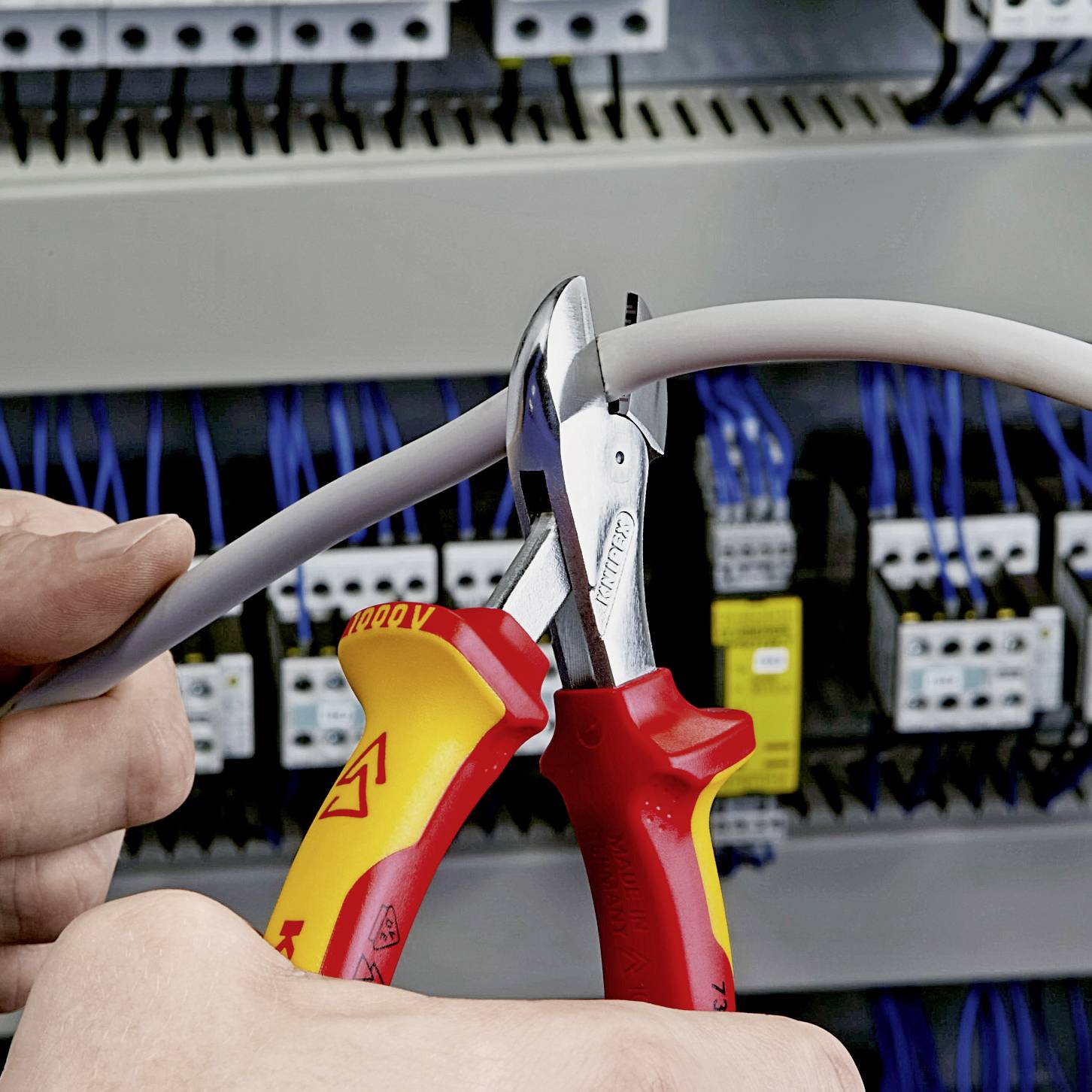 En person klipper en elektrisk kabel med en isolerad avbitare i en elcentral.