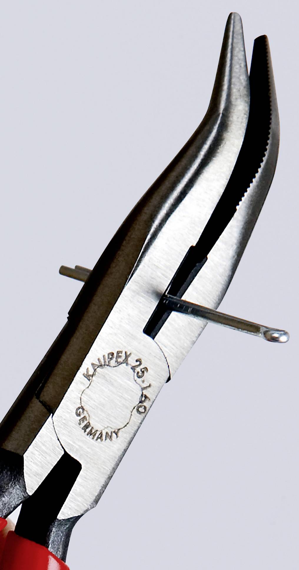 En tång med rött handtag håller en spik. På tången står det 'Knipex 25 140 Germany'.