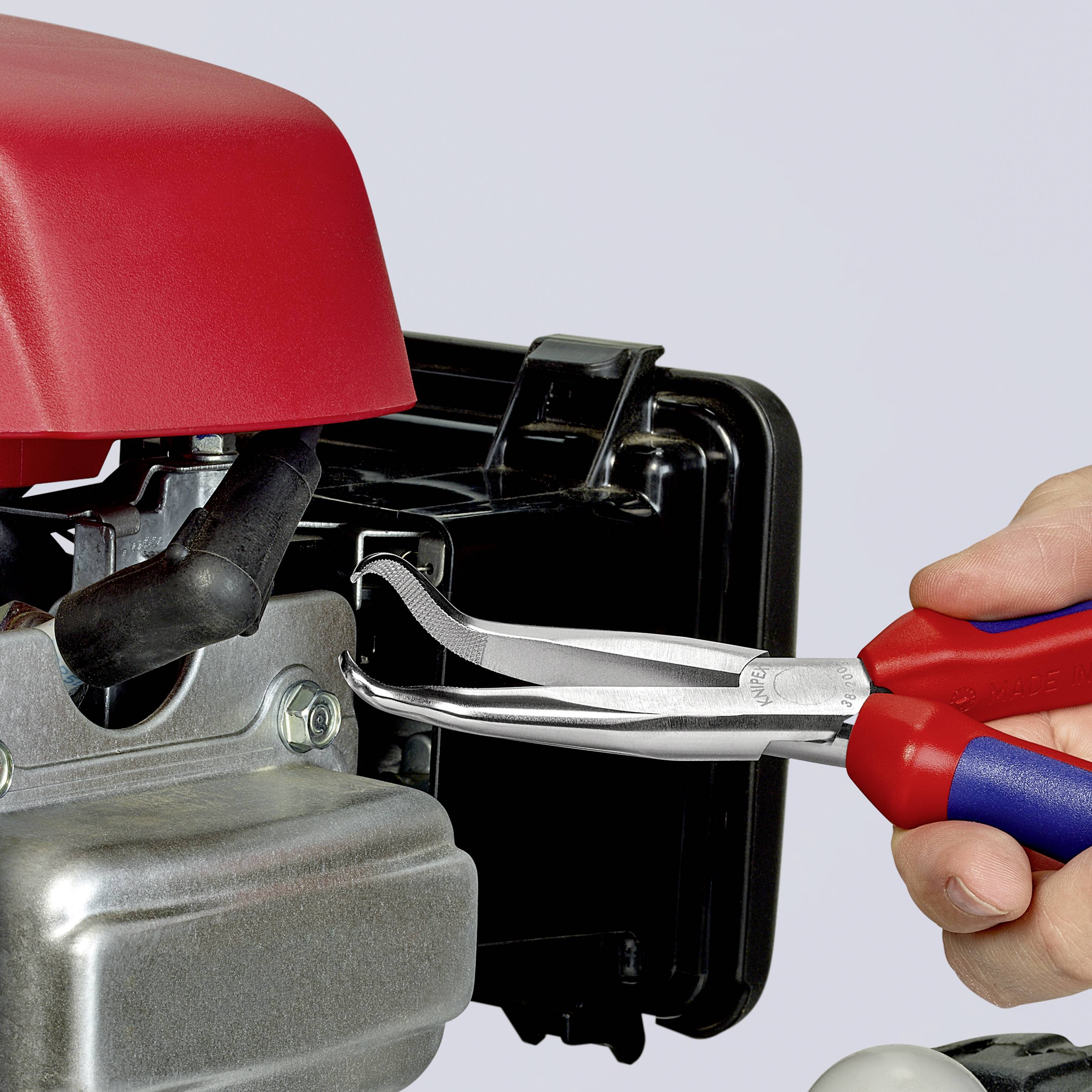 En person håller en röd skiftnyckel för att fästa en slang på en liten, röd motor. Motorn har metall- och plastdelar.