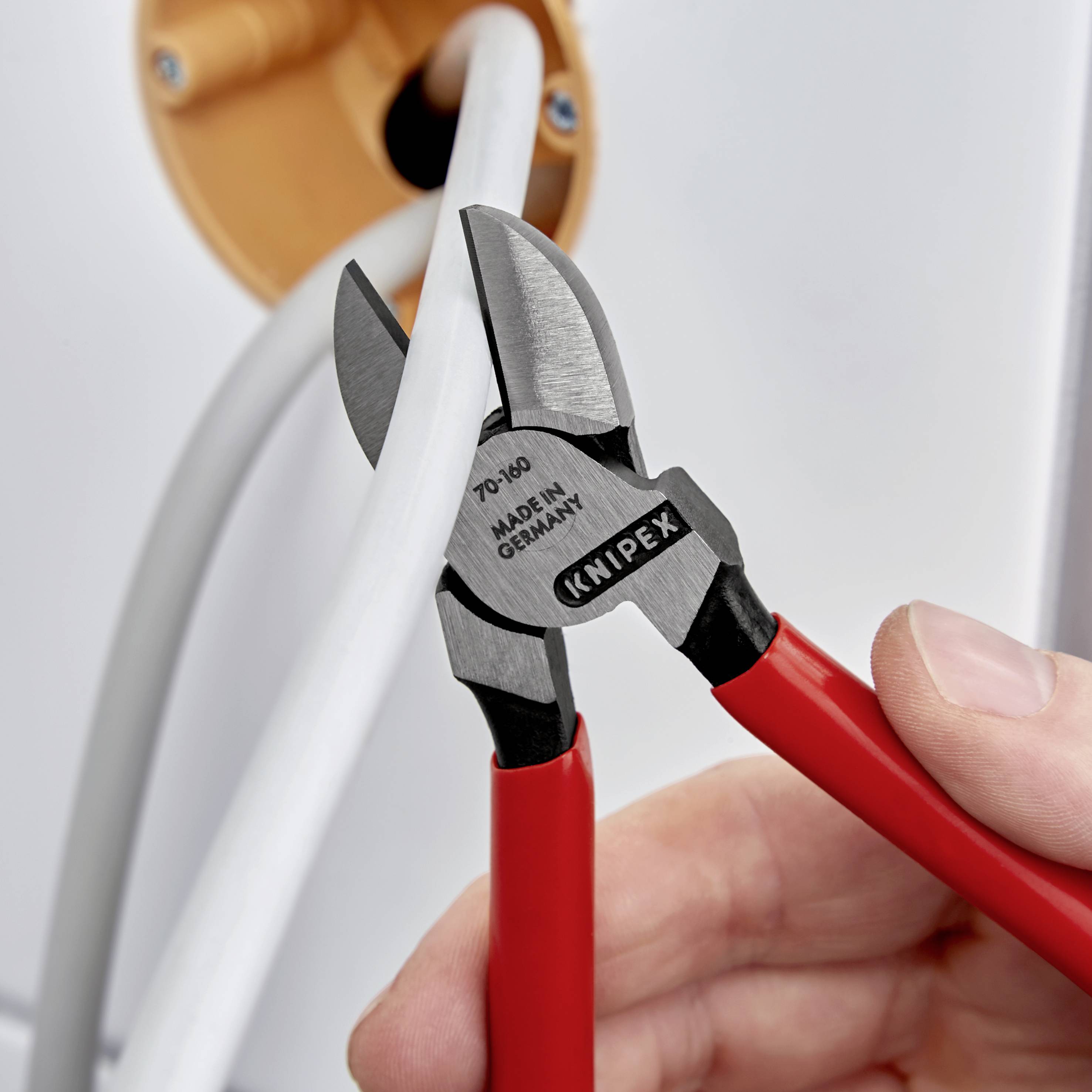 En hand håller en röd kabelsax som klipper av en tjock grå kabel. Saxen är märkt med 'Knipex' och 'Made in Germany'.