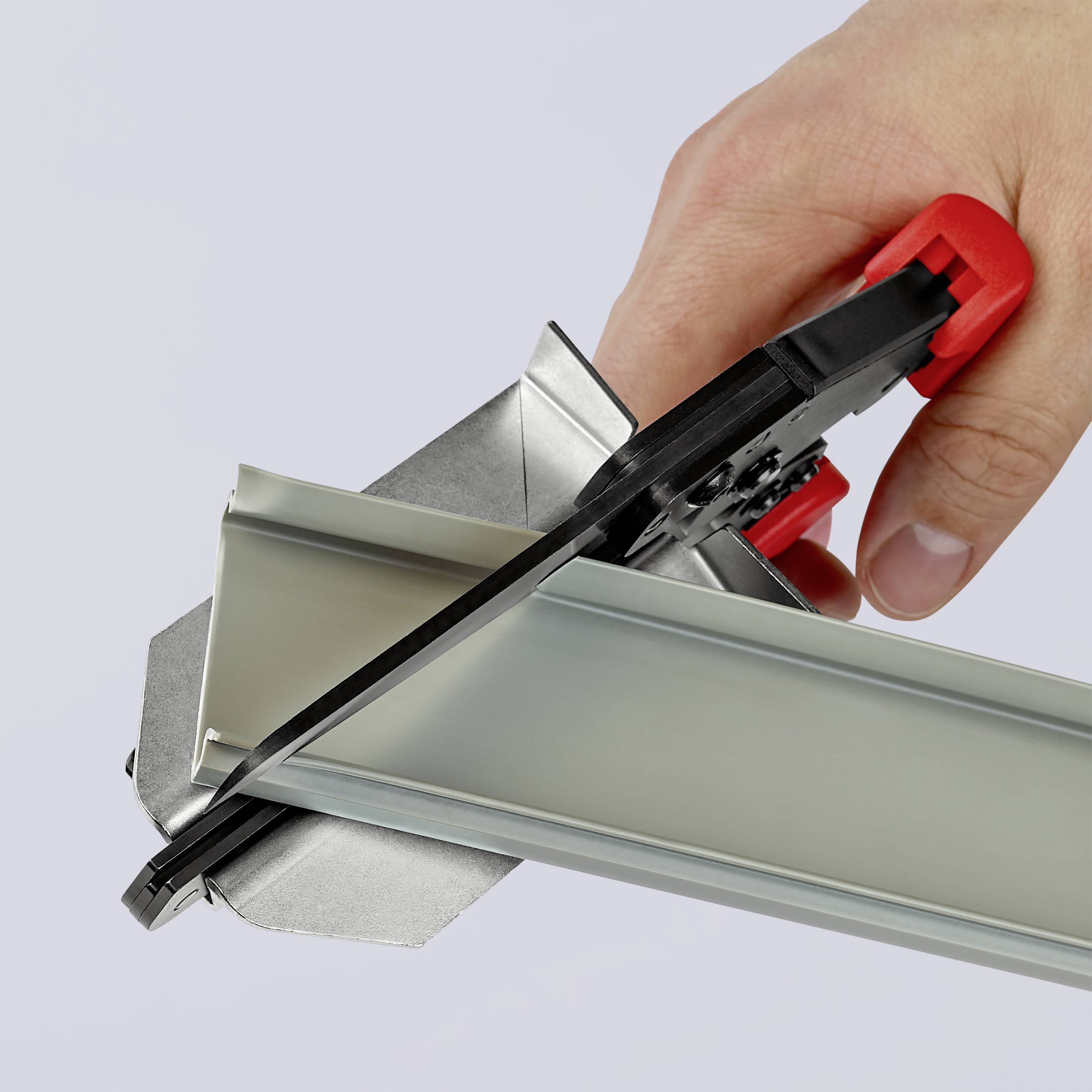 En hand använder en röd och svart skärare för att noggrant kapa ett aluminiumprofilstycke.