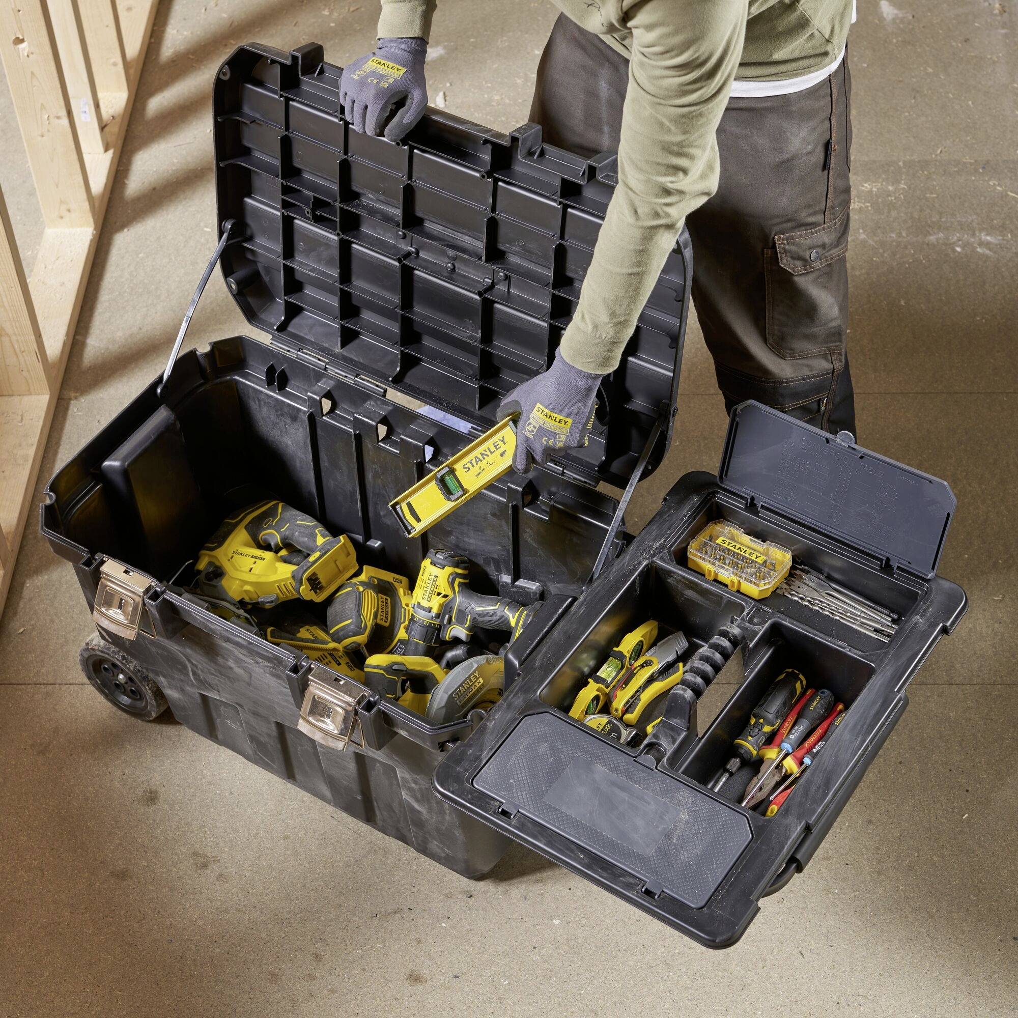 En öppen verktygslåda visar olika elverktyg och tillbehör som borrar och batterier, placerad på en byggarbetsplats.