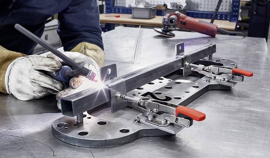 En person svetsar ett metallstycke på en välorganiserad arbetsplats i en verkstad.