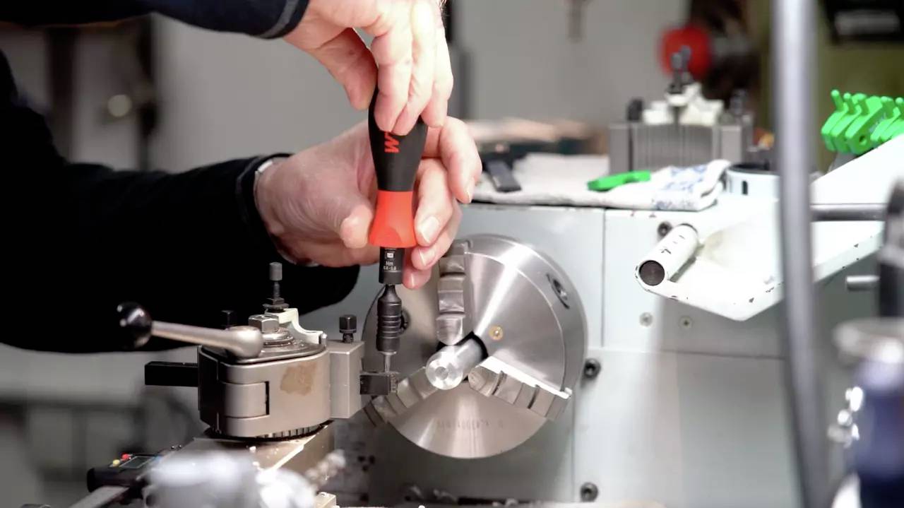 En person använder en skruvmejsel för att justera en metallmaskin. Händer i rörelse. Precisionsarbete inom finmekaniken.