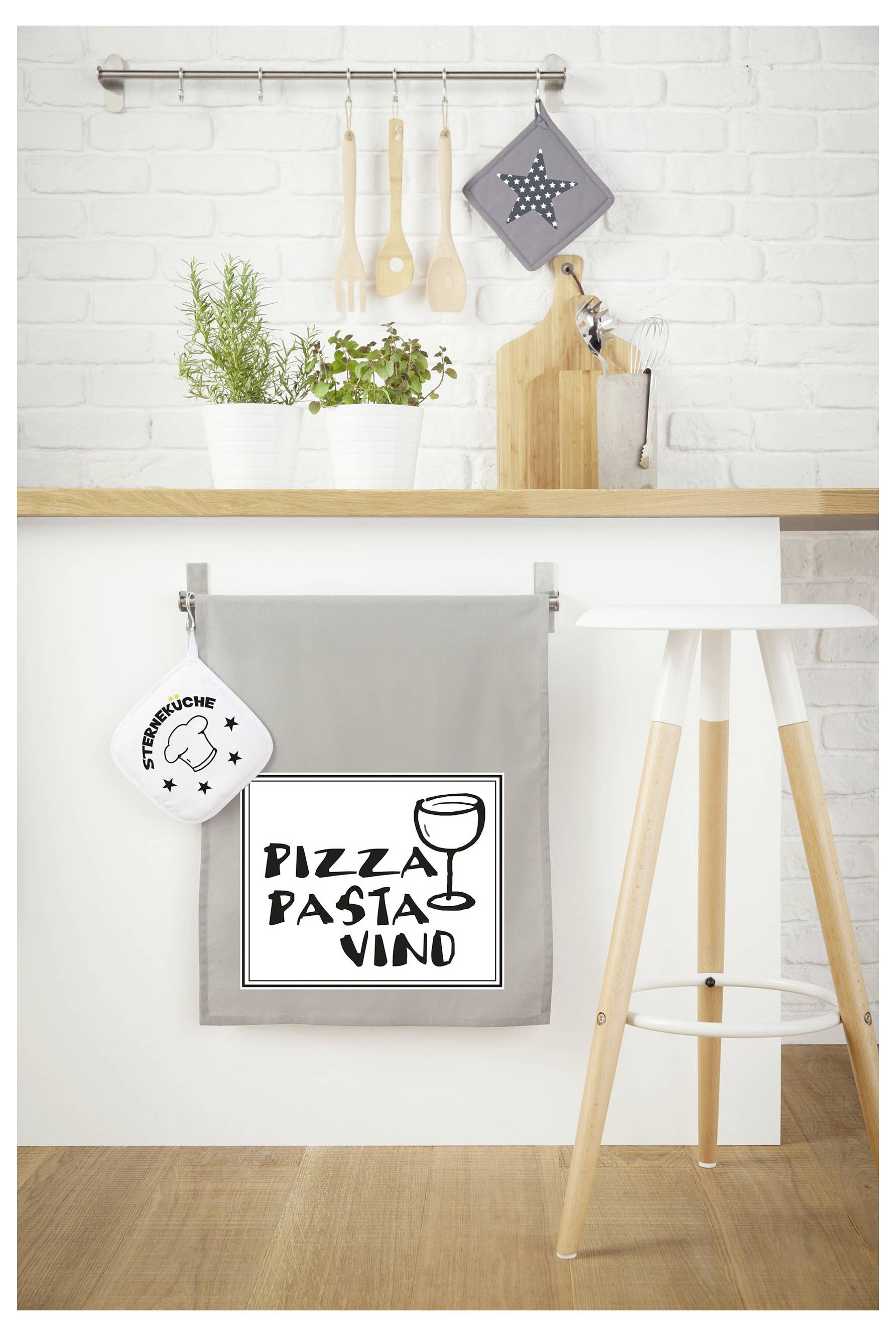 Köksdekorering med hängande köksredskap och krukväxter; längst ned en grå duk med skylt "PIZZA PASTA VINO" på en träö.