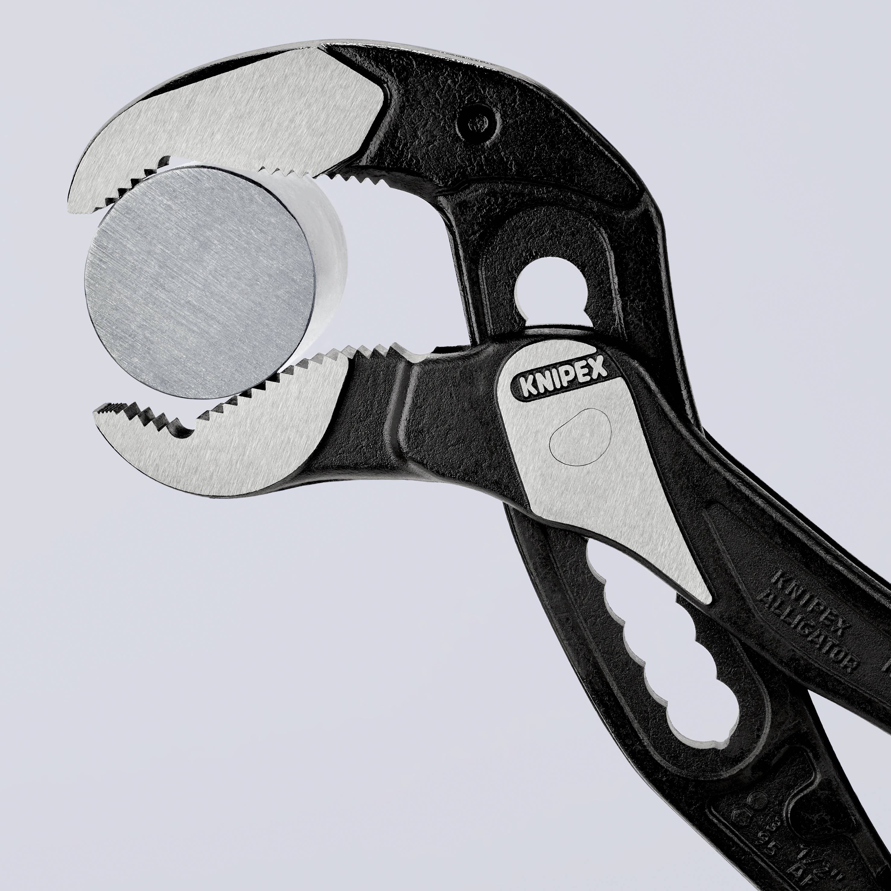 En svart Knipex-tång håller ett rundformat, metalliskt glänsande föremål, sannolikt ett mynt, fast i sitt grepp.