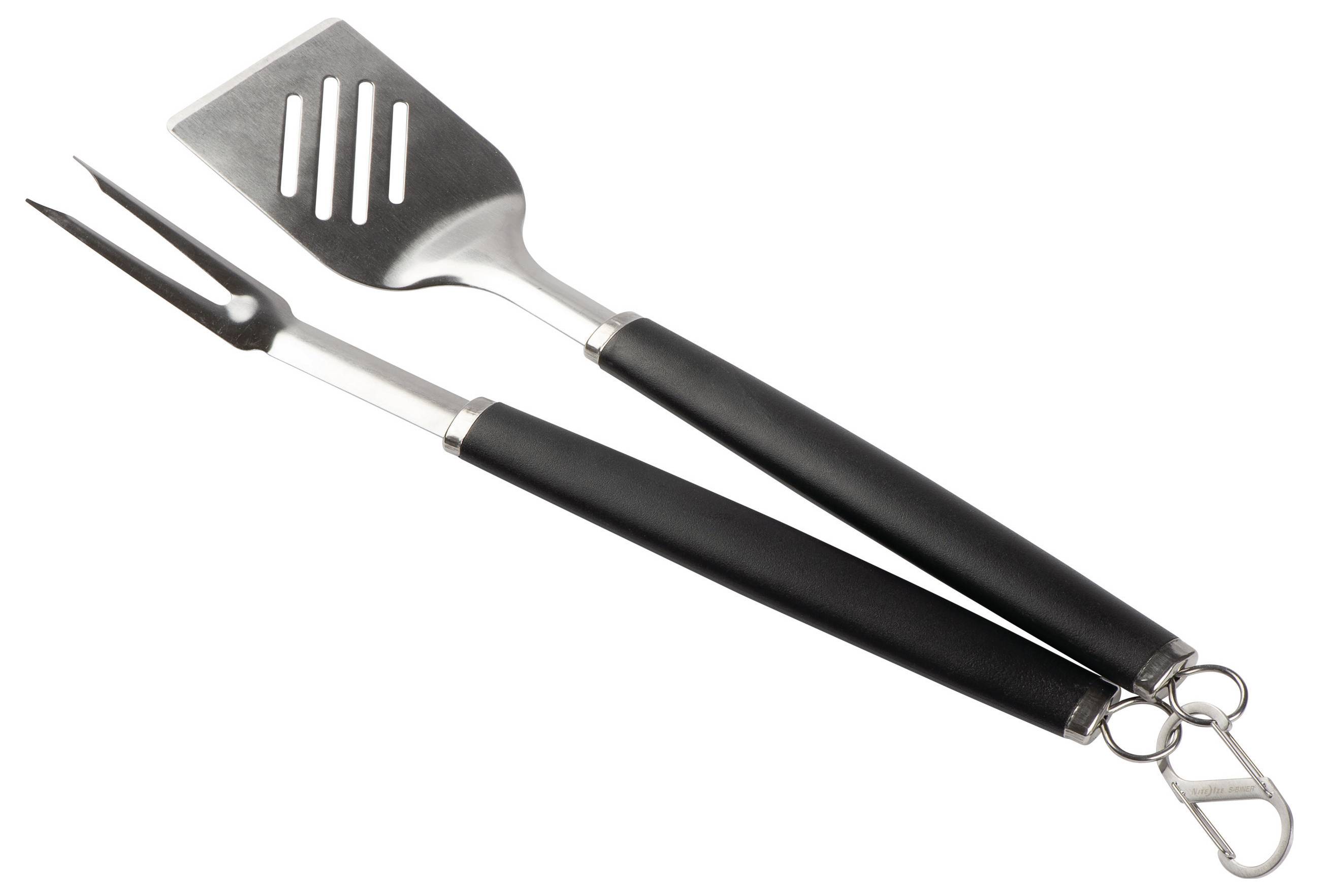 En grillspatel och gaffel i metall med svarta handtag ligger korslagda mot varandra på en vit bakgrund.