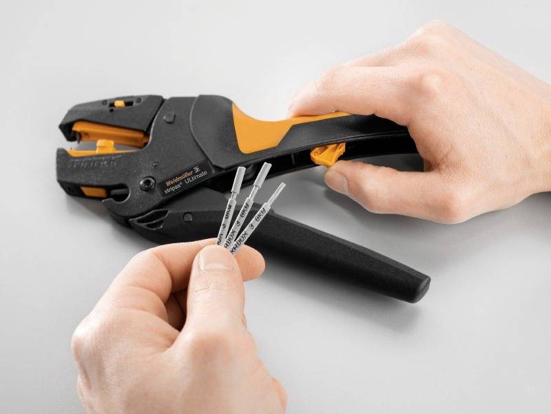 En person håller ett avisoleringsverktyg i vänster hand och trådar i höger hand. Bakgrunden är neutral.