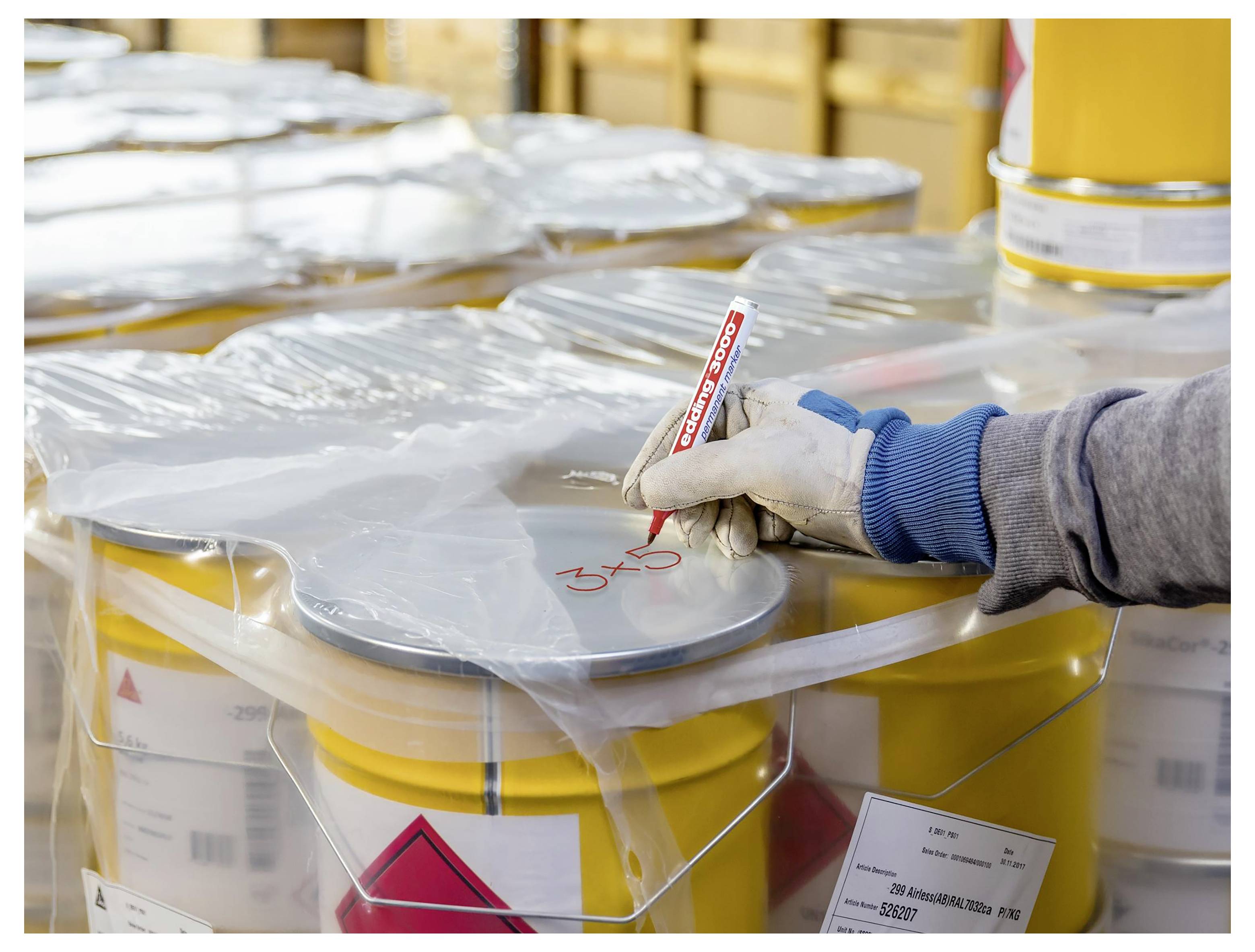 Handsked arbetare märker en förseglar behållare för farligt material med en röd markör i ett lagringsområde.