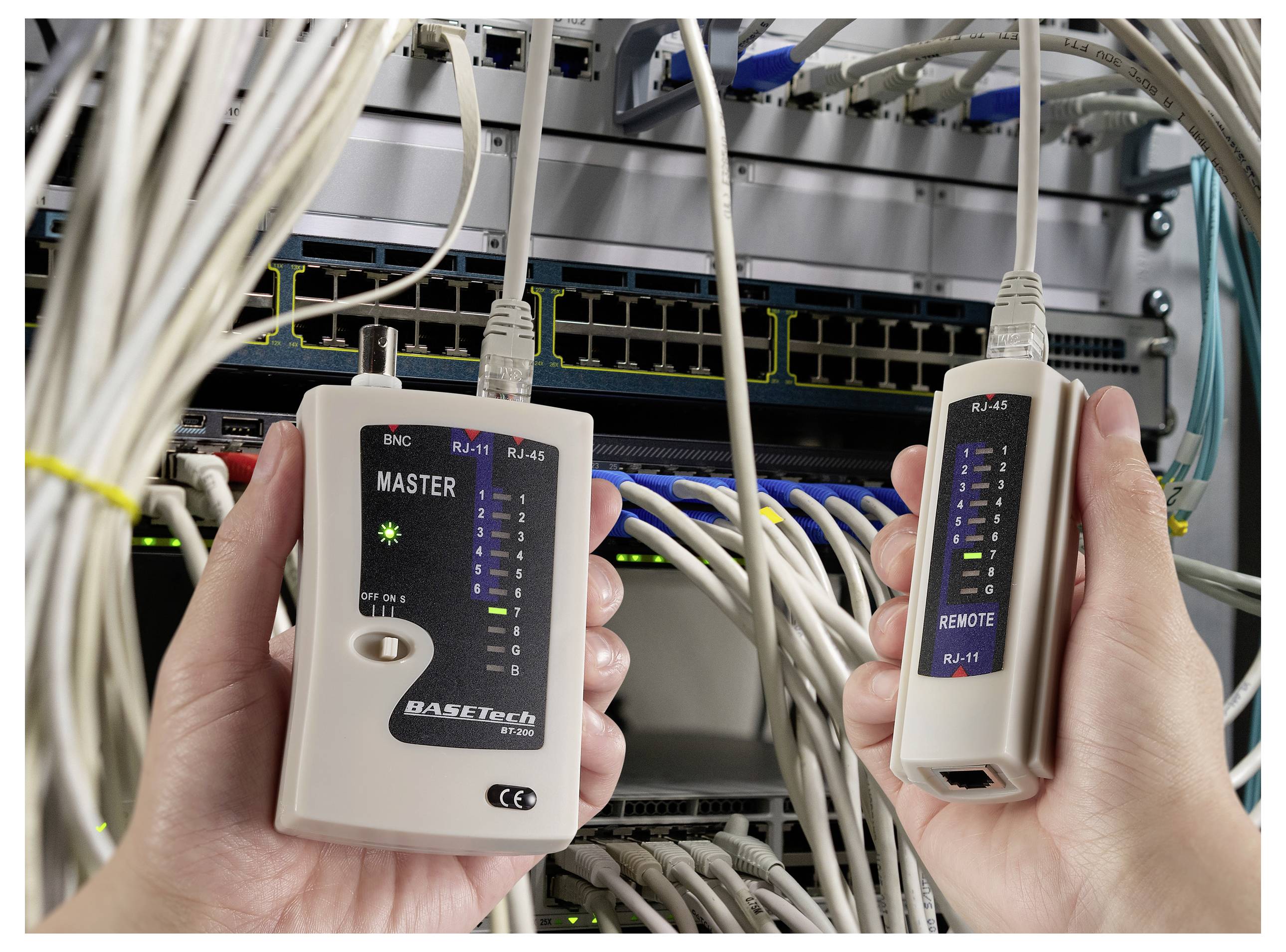 Händer som håller en nätverkskabeltestare framför en serverställning, med kablar anslutna till nätverksutrustning.