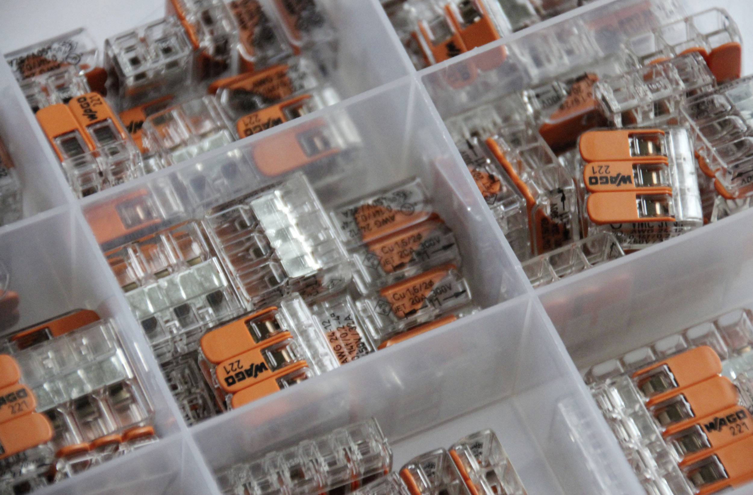 Låda med flera fack, fylld med orangefärgade kabelklämmor för anslutning av elektriska ledare.
