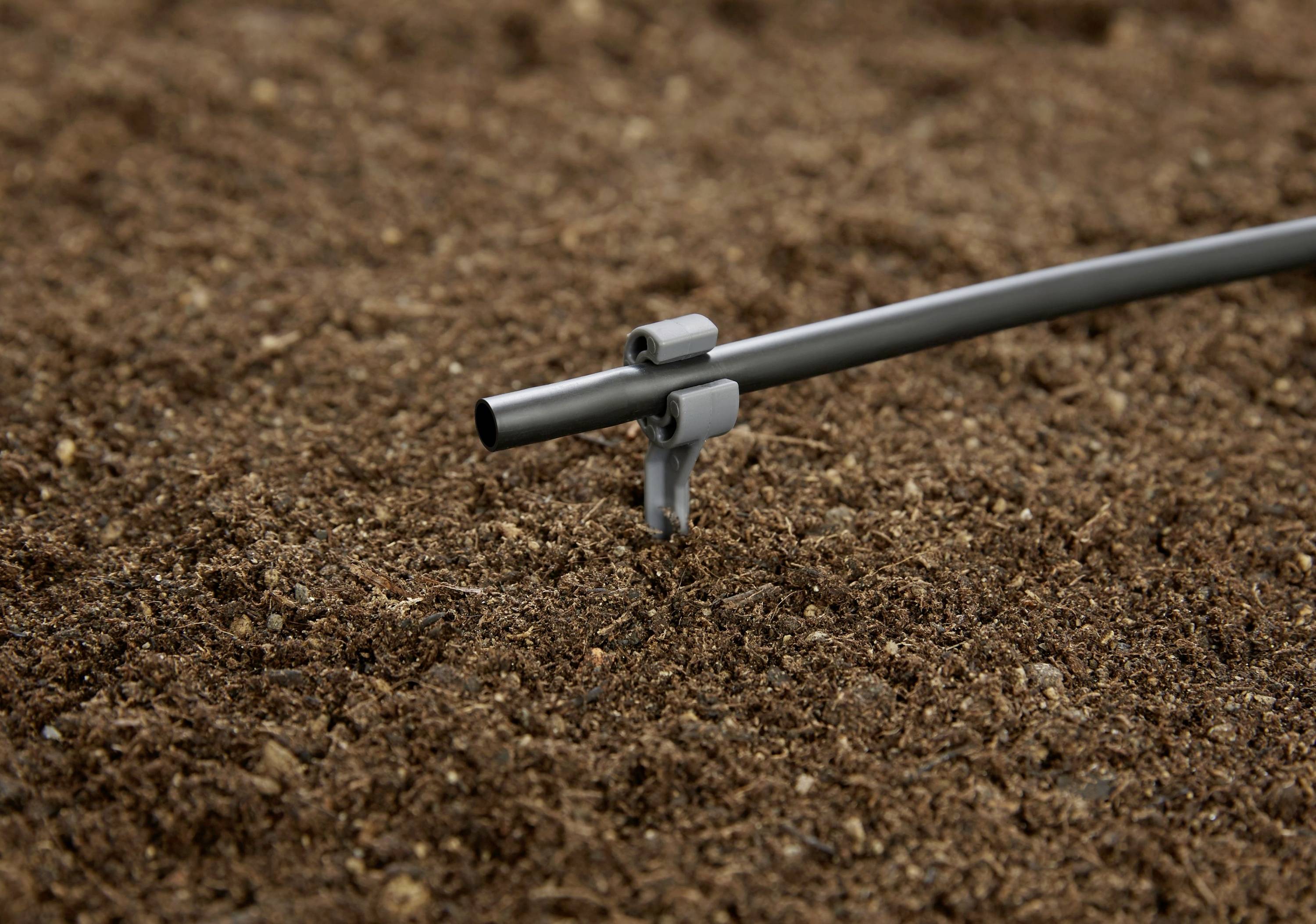 En bevattningsrör med munstycke i marken visar en droppbevattningsanordning som används för riktad bevattning av växter.
