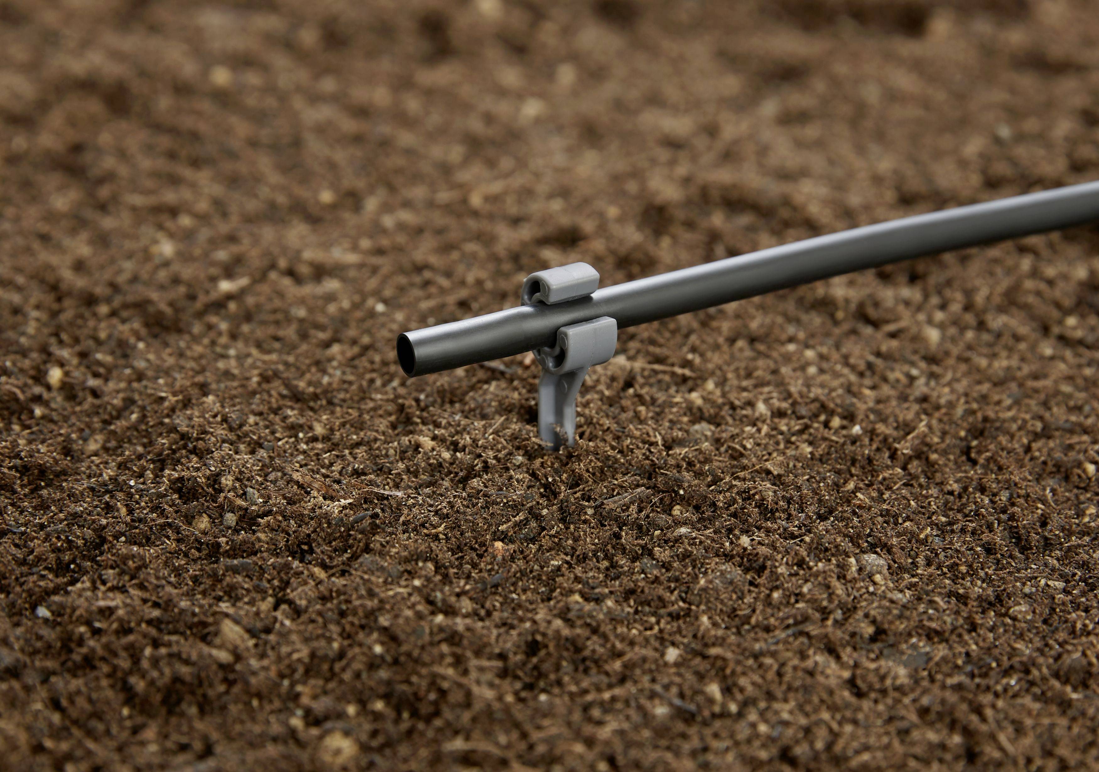 Ett grått bevattningsrör sticker upp ur den bruna jorden, redo att vattna växterna i trädgården.