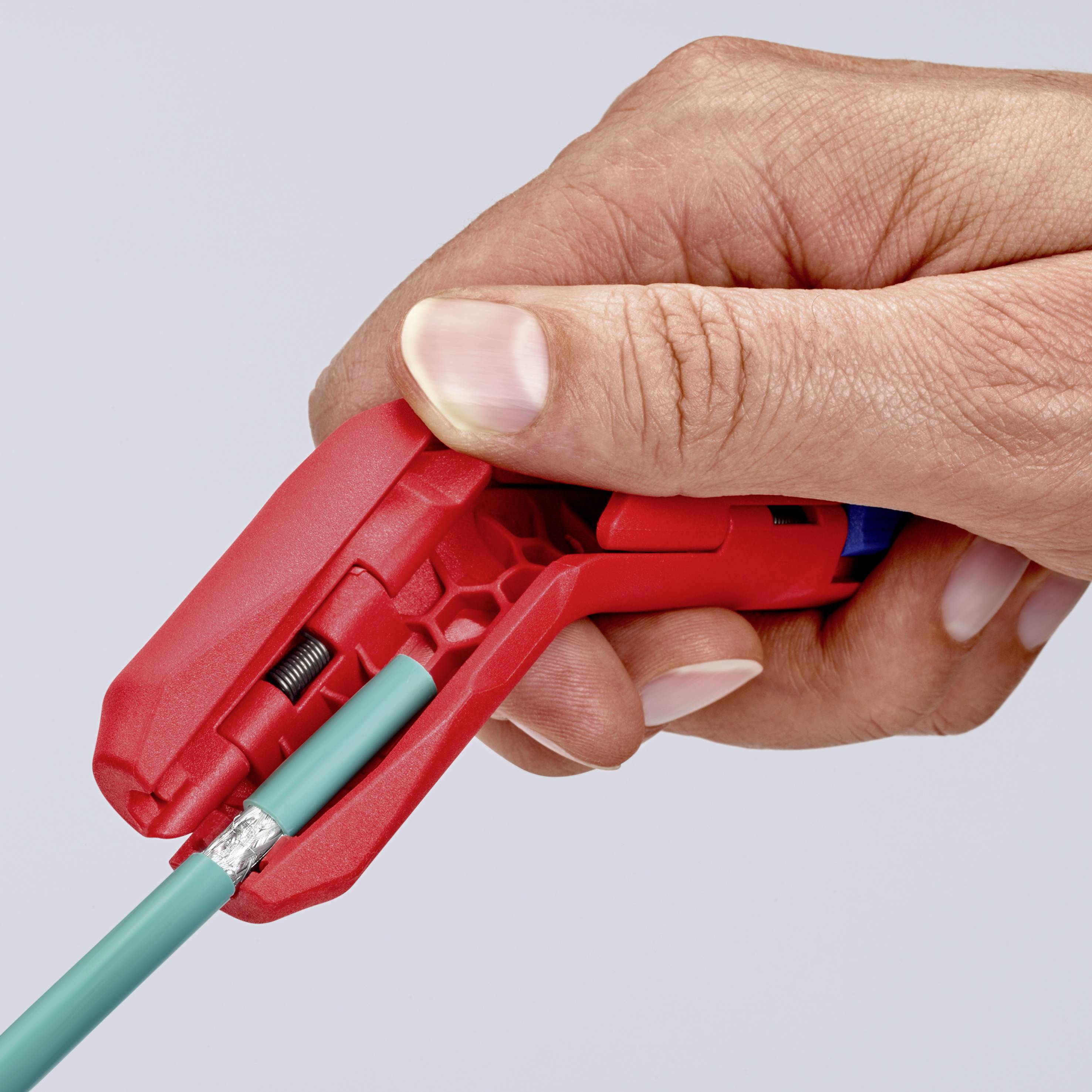 En hand håller ett avisoleringsverktyg som klipper av en röd kabel. Bilden visar avisoleringen i aktion.