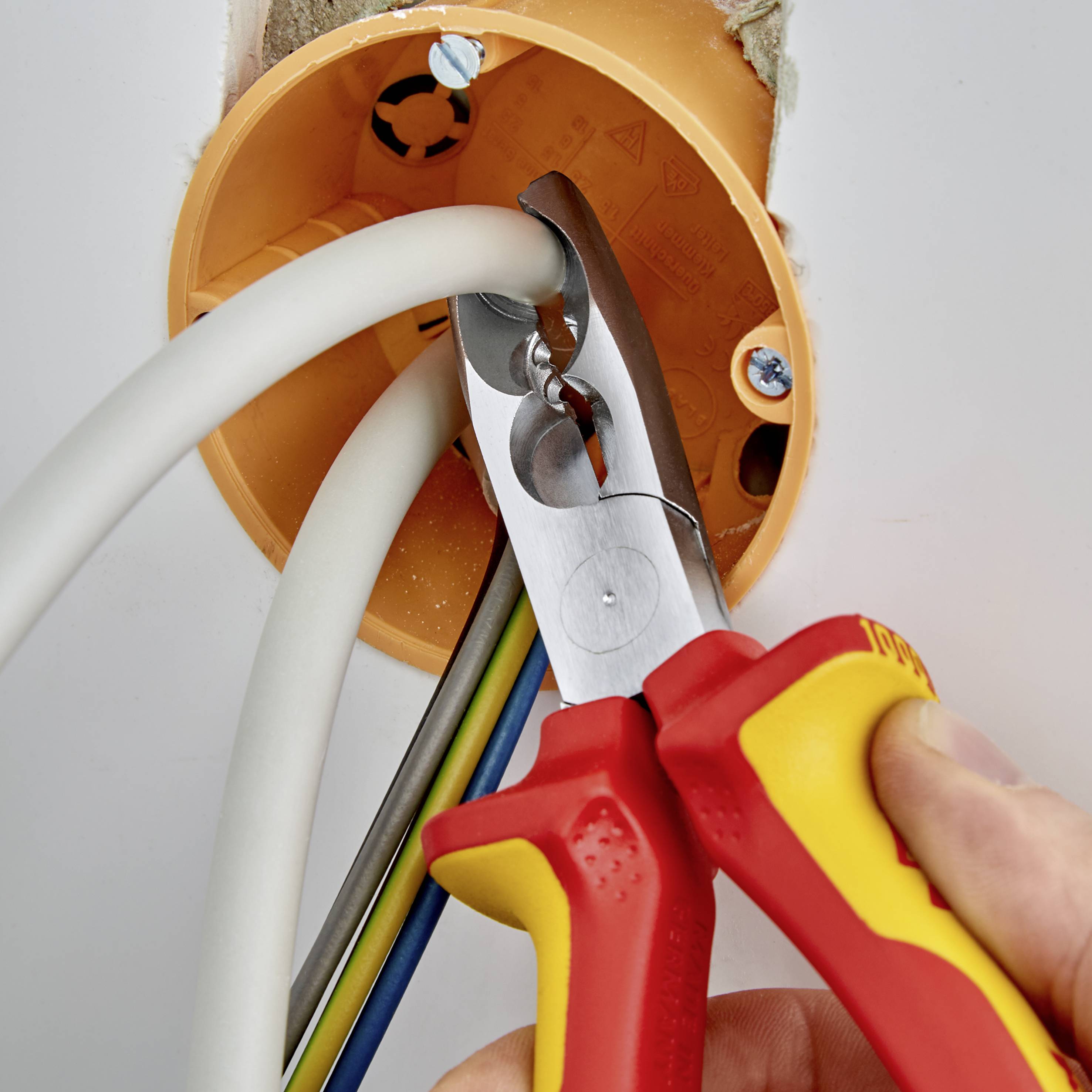 En person drar elektriska kablar genom ett orangefärgat rör med en röd avbitare.