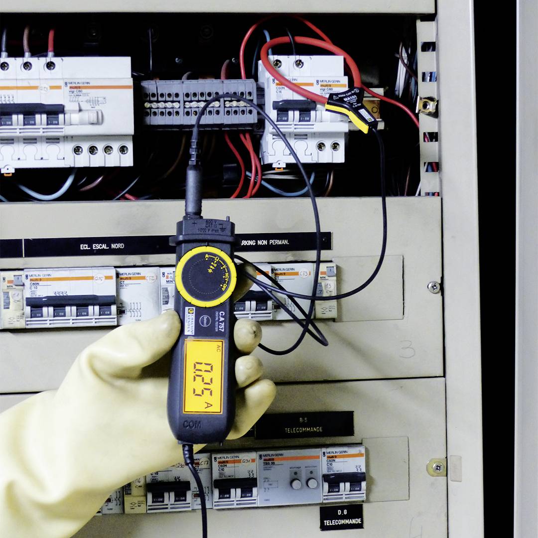 En person mäter strömflödet i en elkopplingsbox med ett digitalt multimeter. Displayen visar '0.254'.