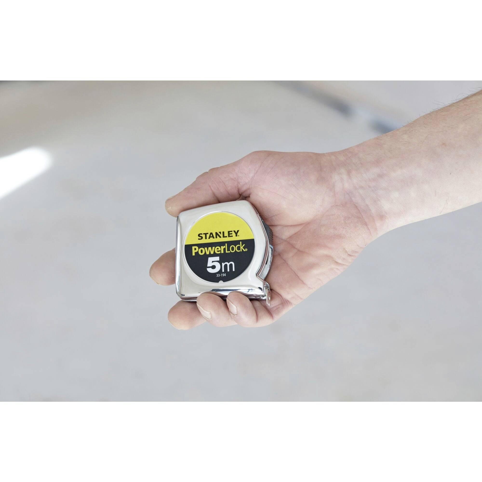 En hand håller ett måttband med texten 'STANLEY PowerLock 5m', redo att användas.