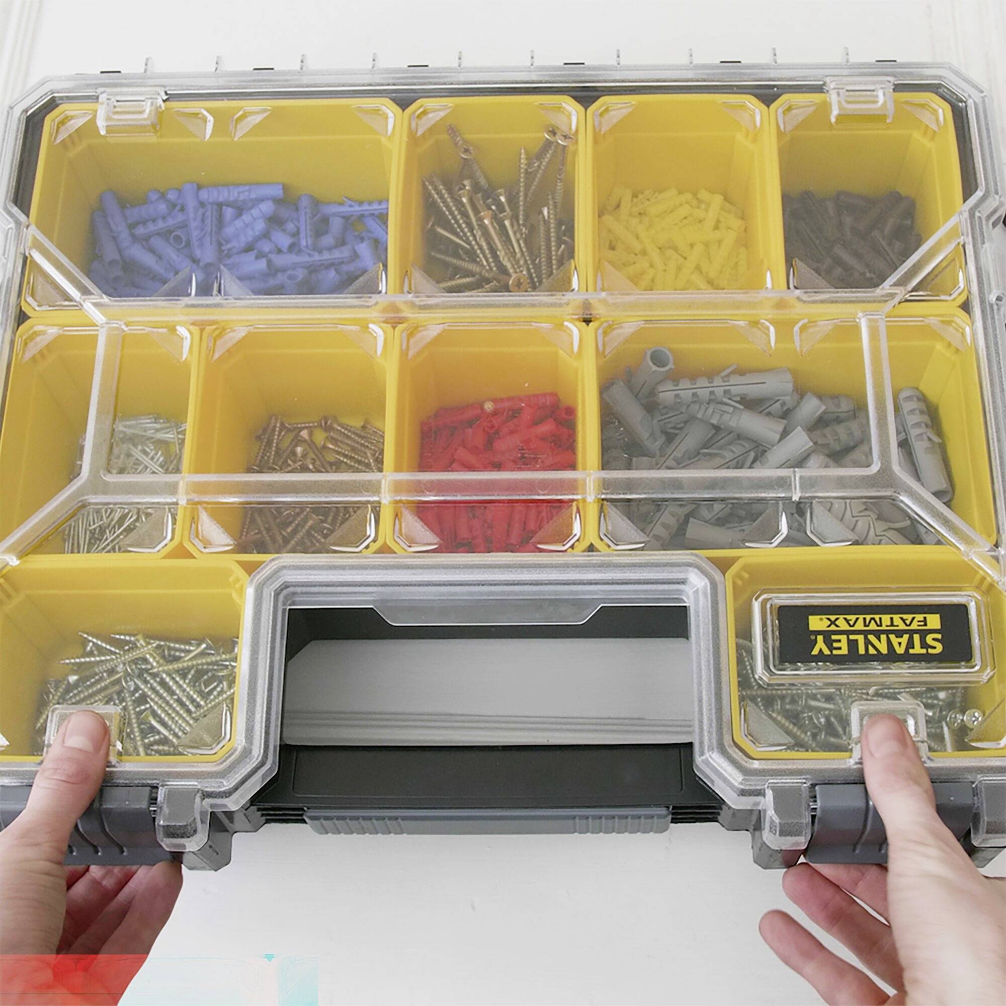 Öppen sorteringsbox med olika skruvar och pluggar i gula fack. Två händer håller boxen.