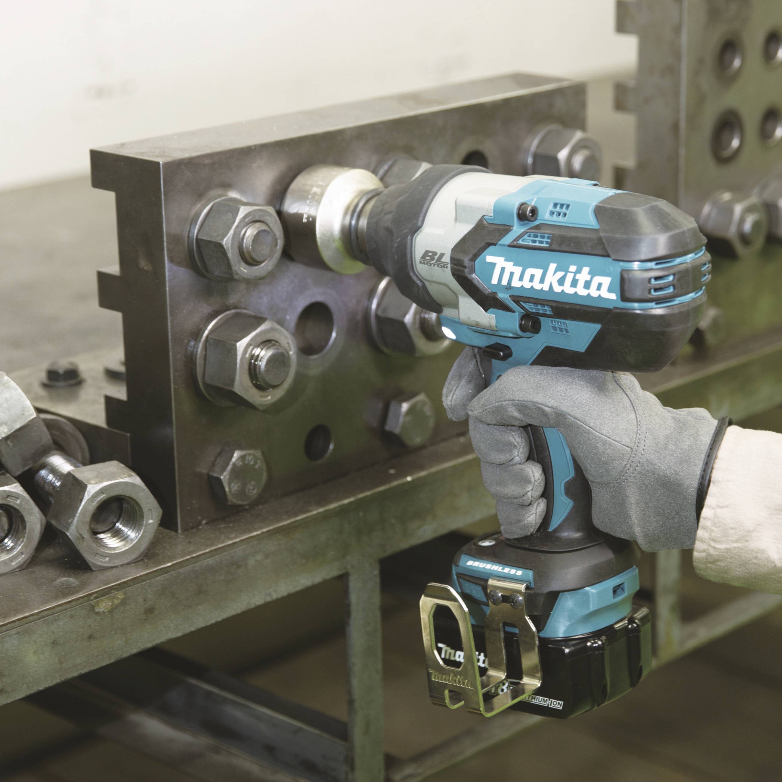 En person fäster en metallplatta med en sladdlös Makita slagskruvmejsel. Skruvar och muttrar är synliga.