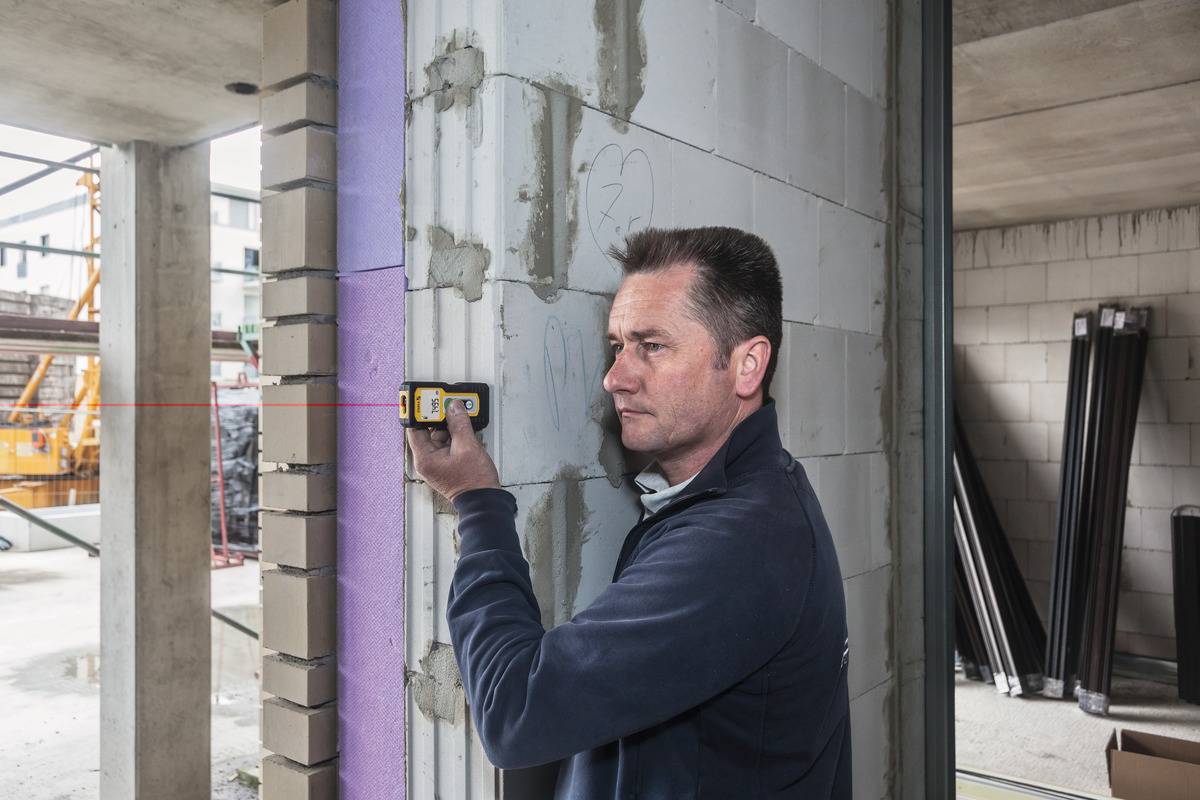 En man använder ett lasermätinstrument för att mäta bredden på en vägg i en oavslutad byggnad.