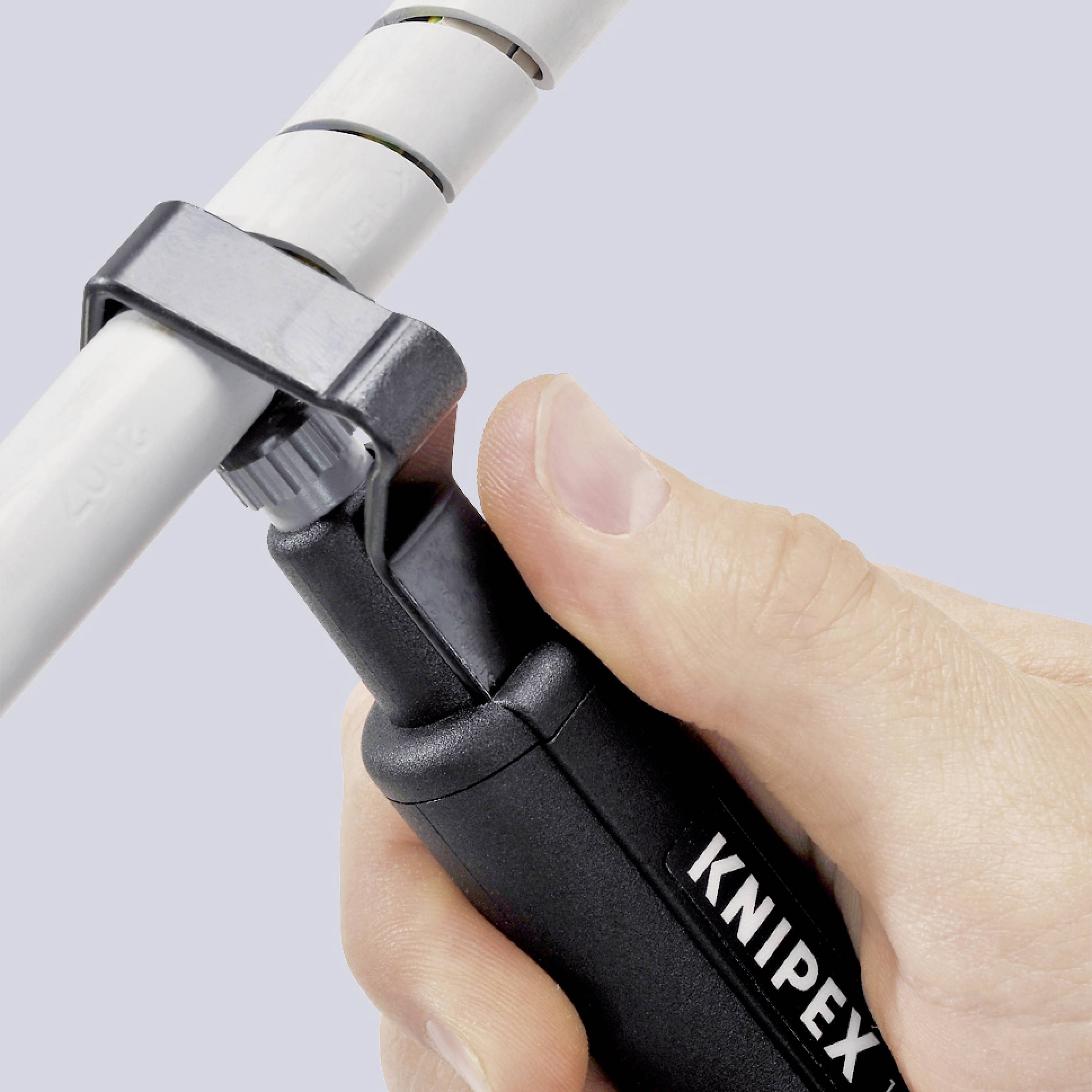 En hand använder ett KNIPEX-verktyg för att noggrant avisolera en kabel genom ett spår i styrningsanordningen.