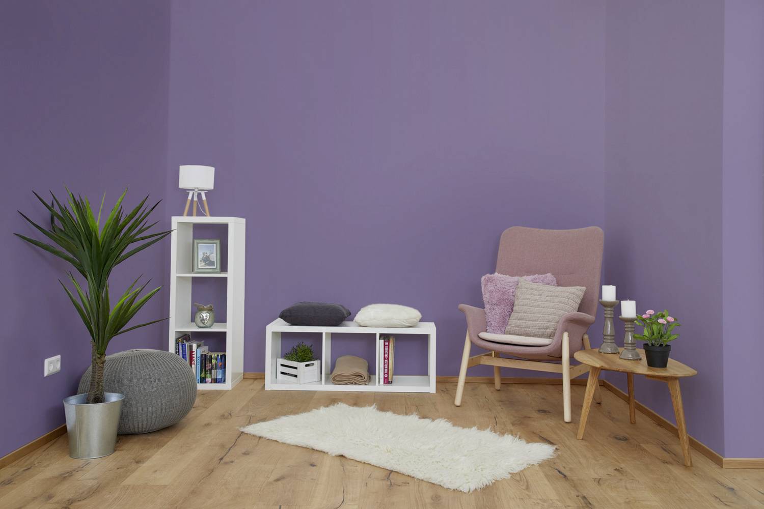 Mysigt vardagsrum med lila väggar, en rosa fåtölj, en vit bokhylla och en krukväxt. Skandinavisk design.