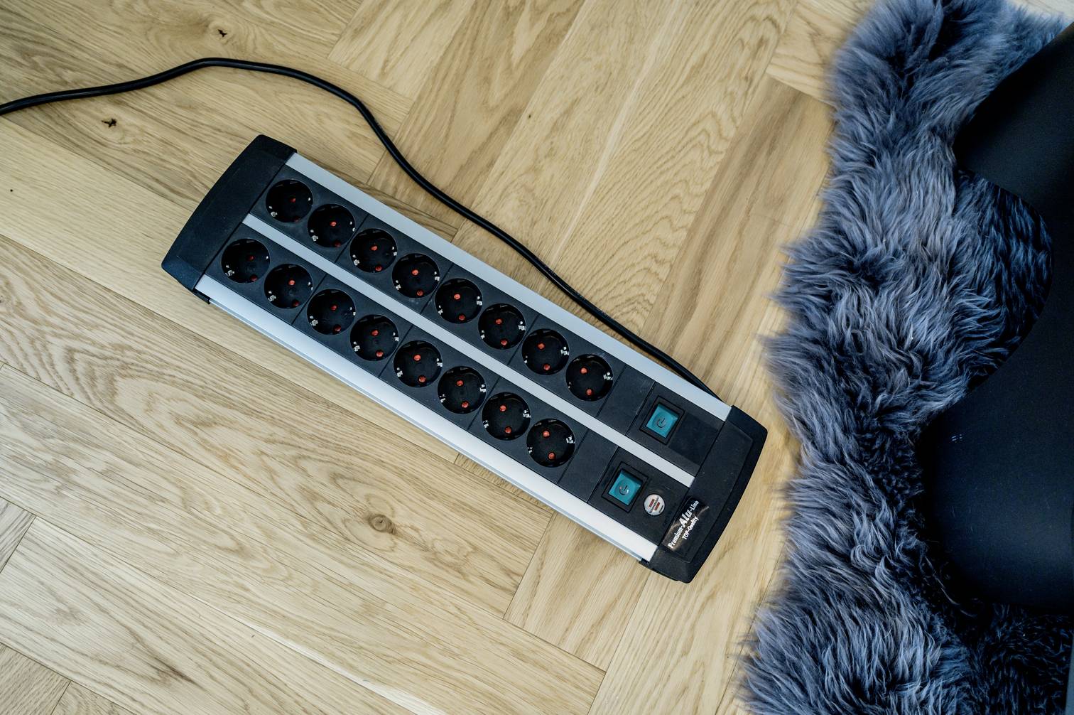 Ett grenuttag med flera uttag ligger på ett trägolv bredvid en grå ullmatta.