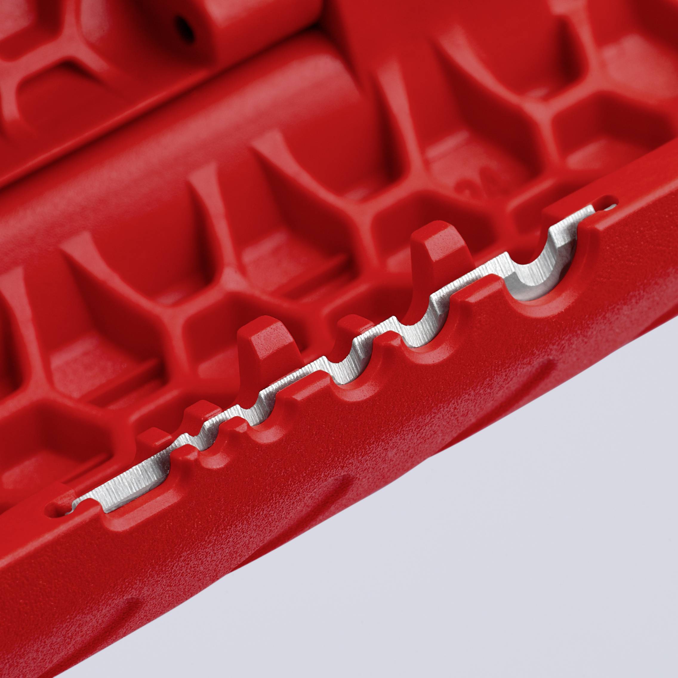 Närbild av en röd, strukturerad yta med en vågformad metallkant som visar ett tekniskt föremål.
