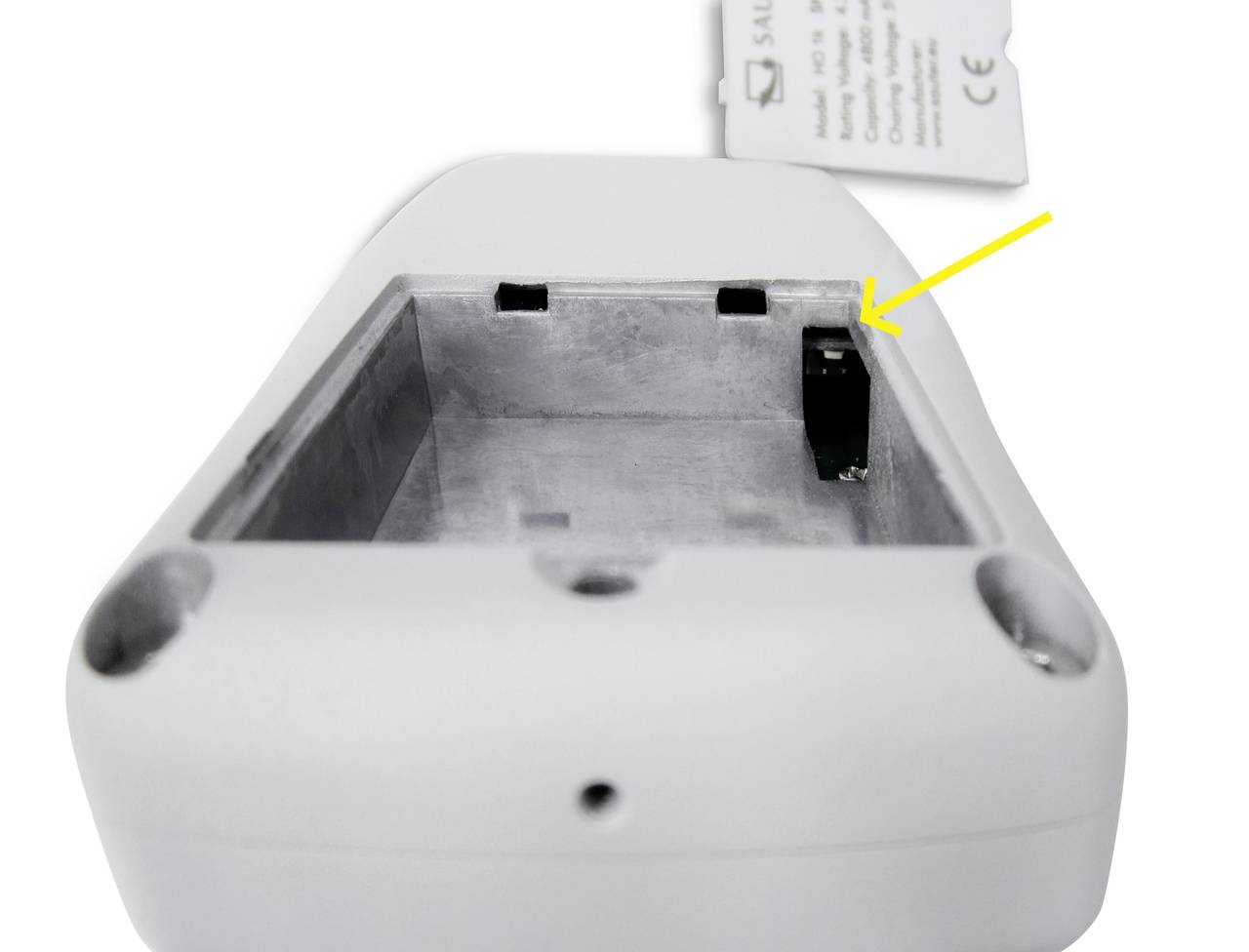 Undersidan av en enhet med batterilucka. En gul pil pekar på en svart switch i batterifacket.