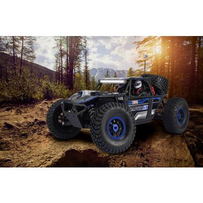 En radiostyrd bil i offroad-design på en stenig skogsväg med träd och berg i bakgrunden vid solnedgången.