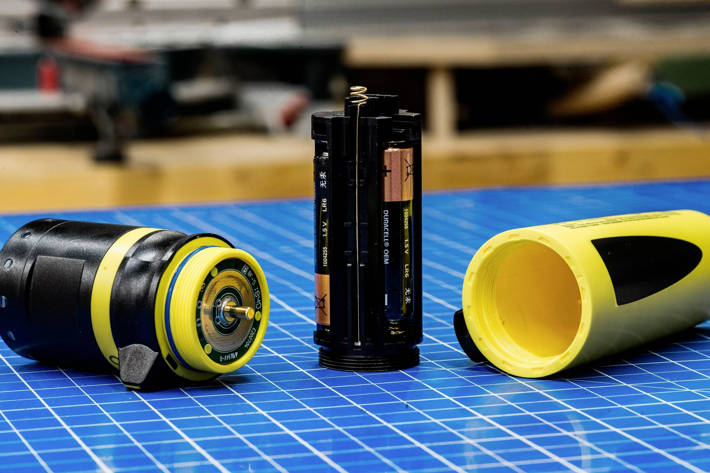 Ett enkelt elektroniskt enhetsapparat med öppna batterifack på ett blått mönstrat bord, klargjort för underhåll eller batteribyte.