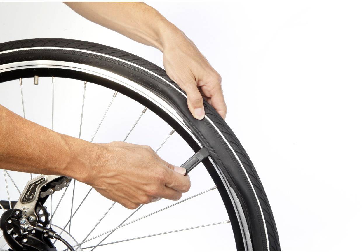 En person byter ett däck på en cykel genom att använda däckavtagare för att lossa däcket från fälgen.