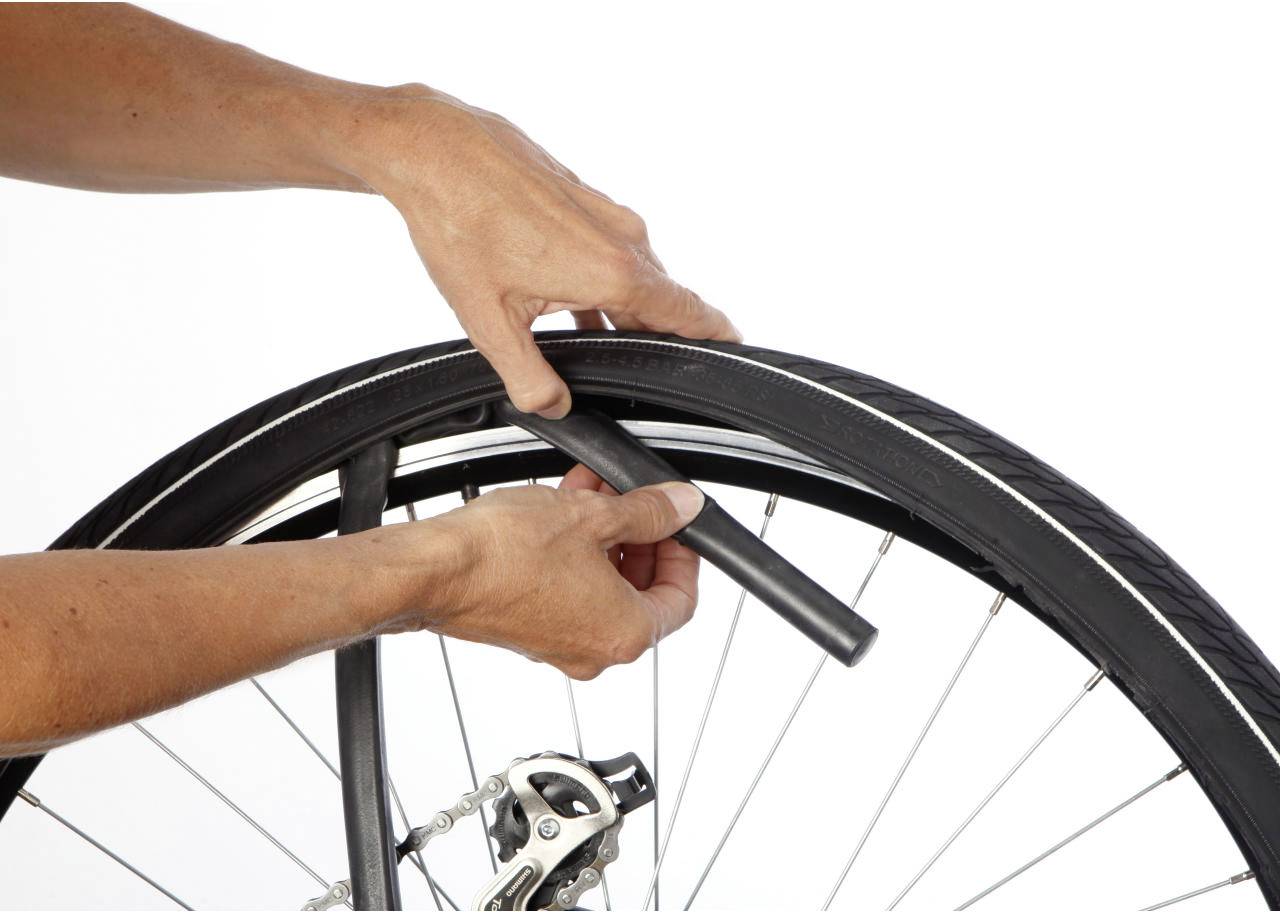 En person byter cykelhjul. Händer tar bort den gamla slangen från ett cykelhjul. I bakgrunden syns bromsen.