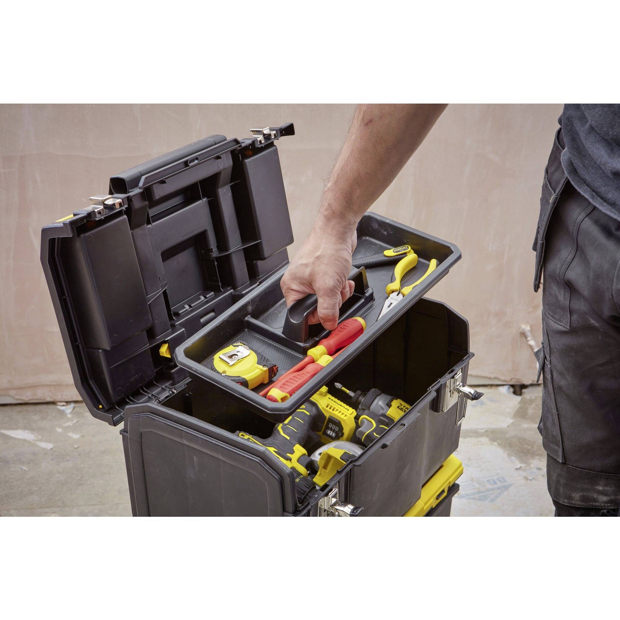 En person plockar verktyg från en öppnad, svart verktygslåda, bland annat en röd skruvmejsel och andra handverktyg.