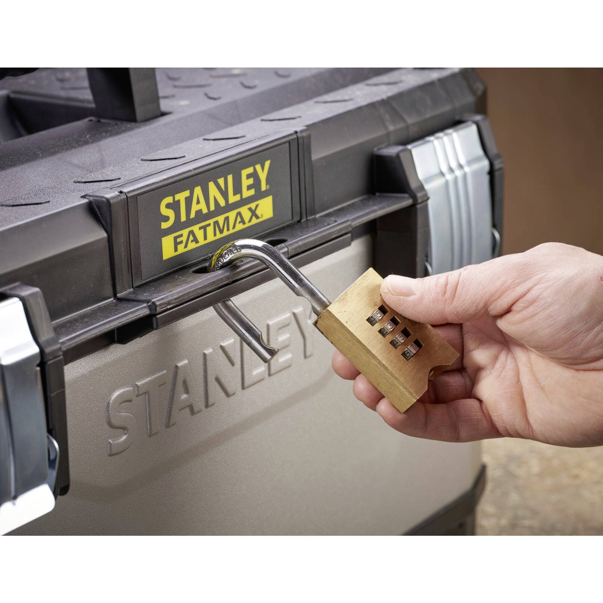 En hand håller ett kombinationslås och öppnar en Stanley-verktygslåda märkt 'STANLEY FATMAX'.